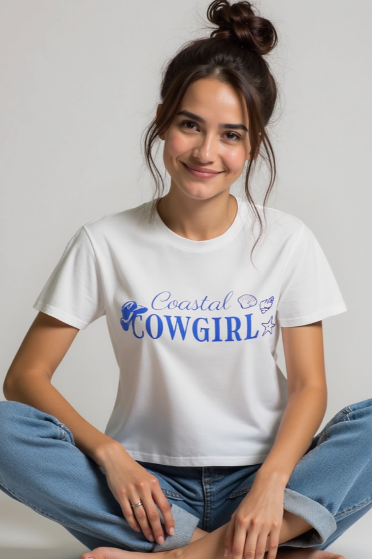 A woman sitting and smiling, wearing a white crop top with &