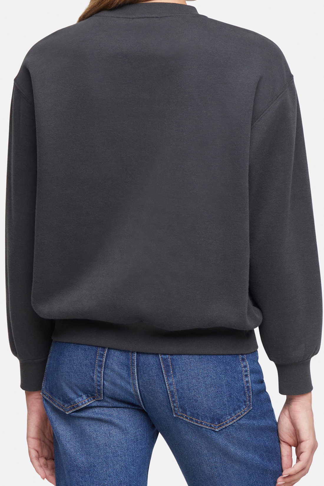 Back of woman wearing a dark gray sweatshirt and blue jeans on a white background