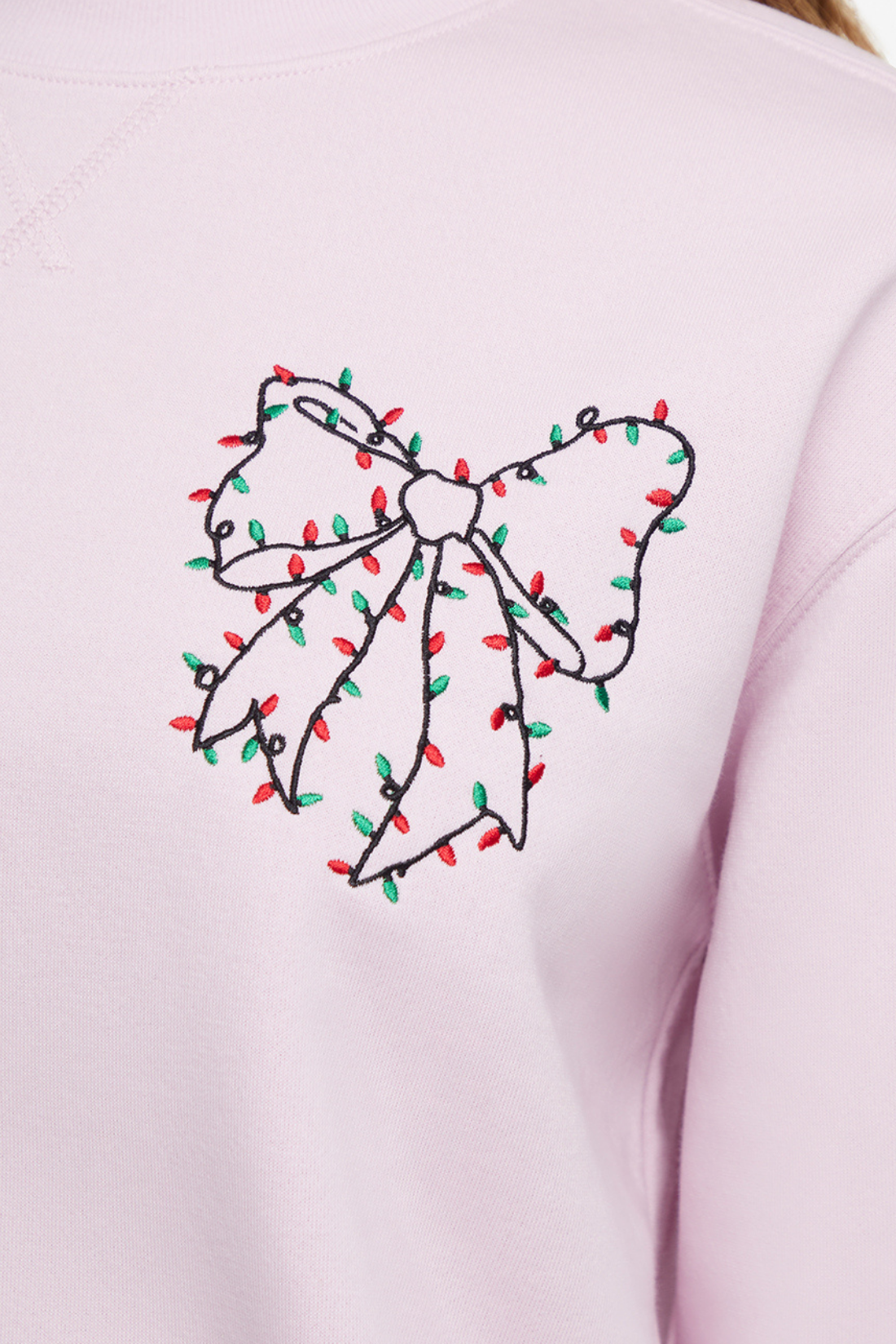 Close up of light pink sweatshirt with a decorative Christmas lights bow design on the back