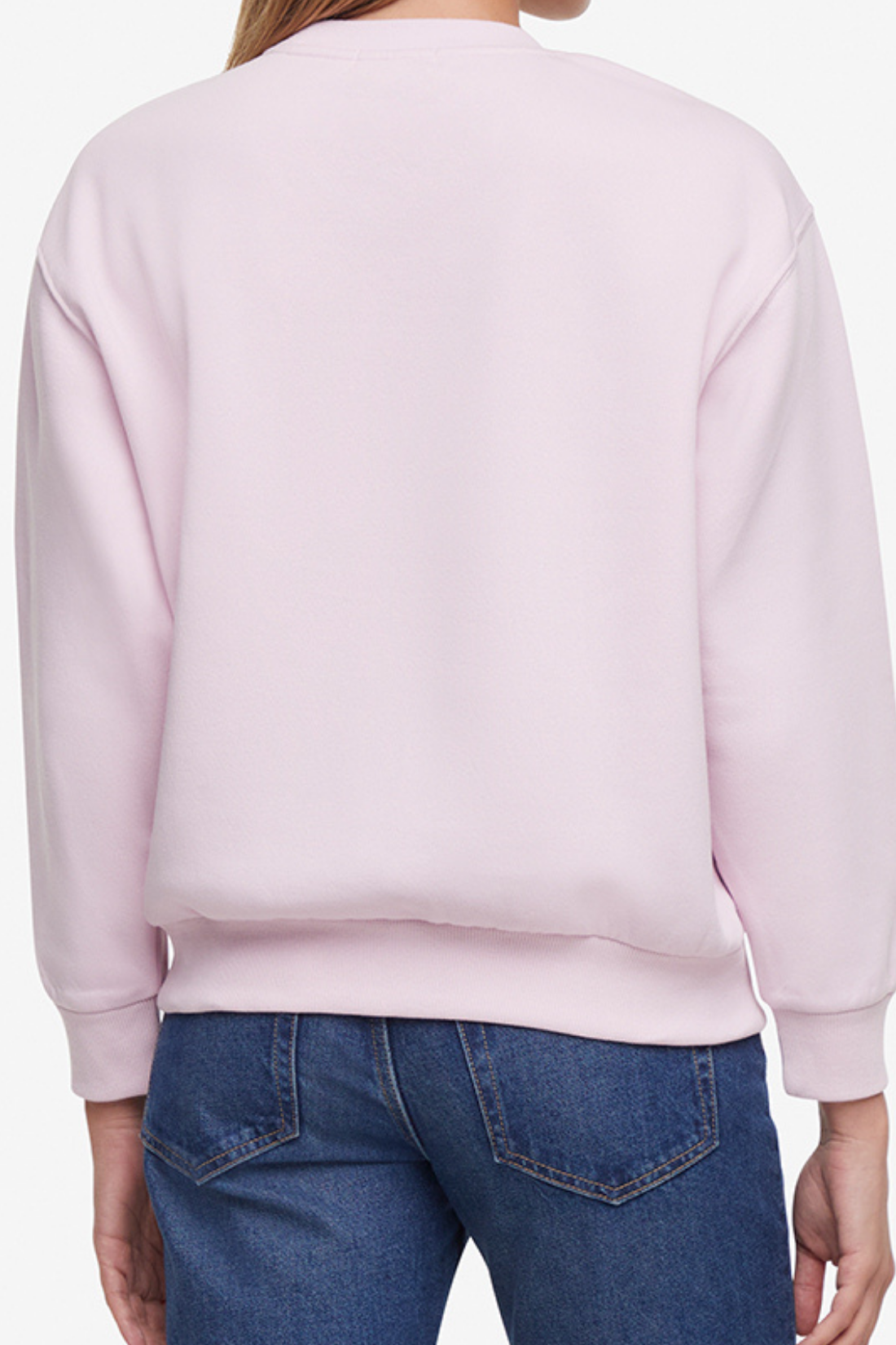 Back of woman wearing a pink sweatshirt and blue jeans on a plain background