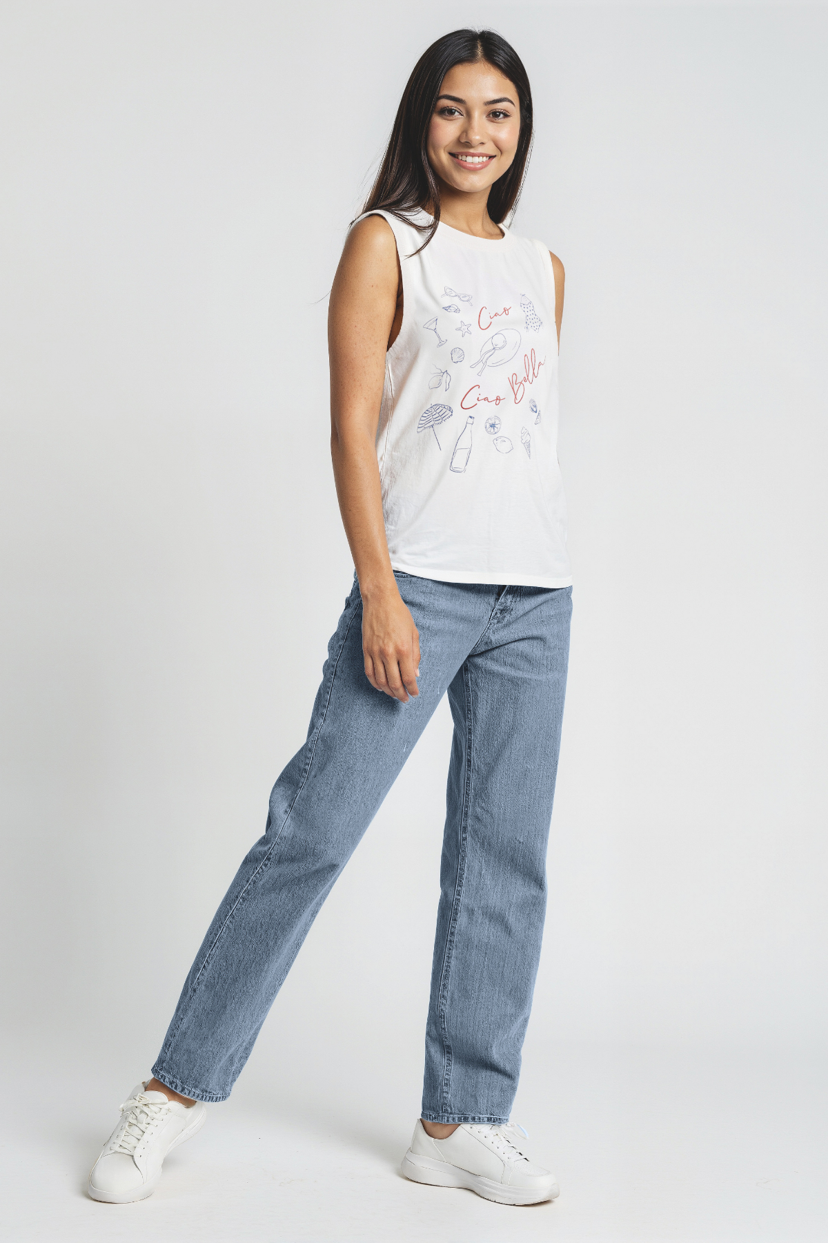 Woman wearing a white sleeveless top with colorful designs and blue jeans on a white background