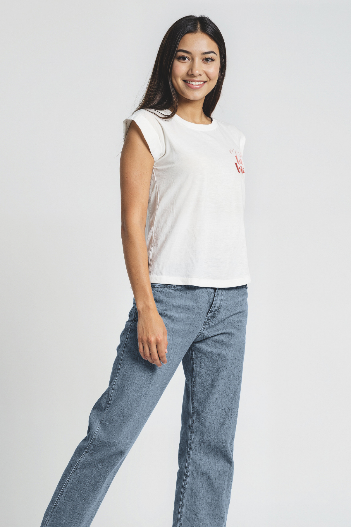 Woman wearing a white t-shirt and blue jeans on a plain background
