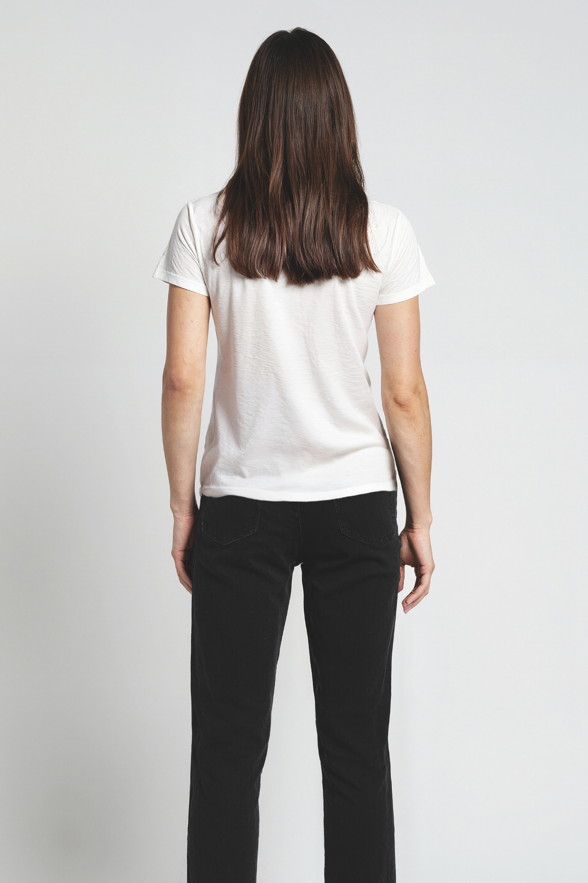 Woman wearing a white t-shirt and black pants on a plain background
