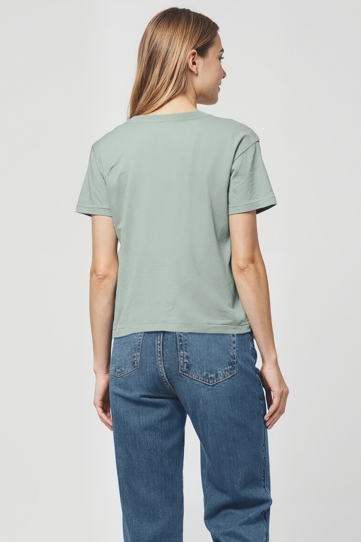 Woman wearing a light green t-shirt and blue jeans on a plain background from the back view