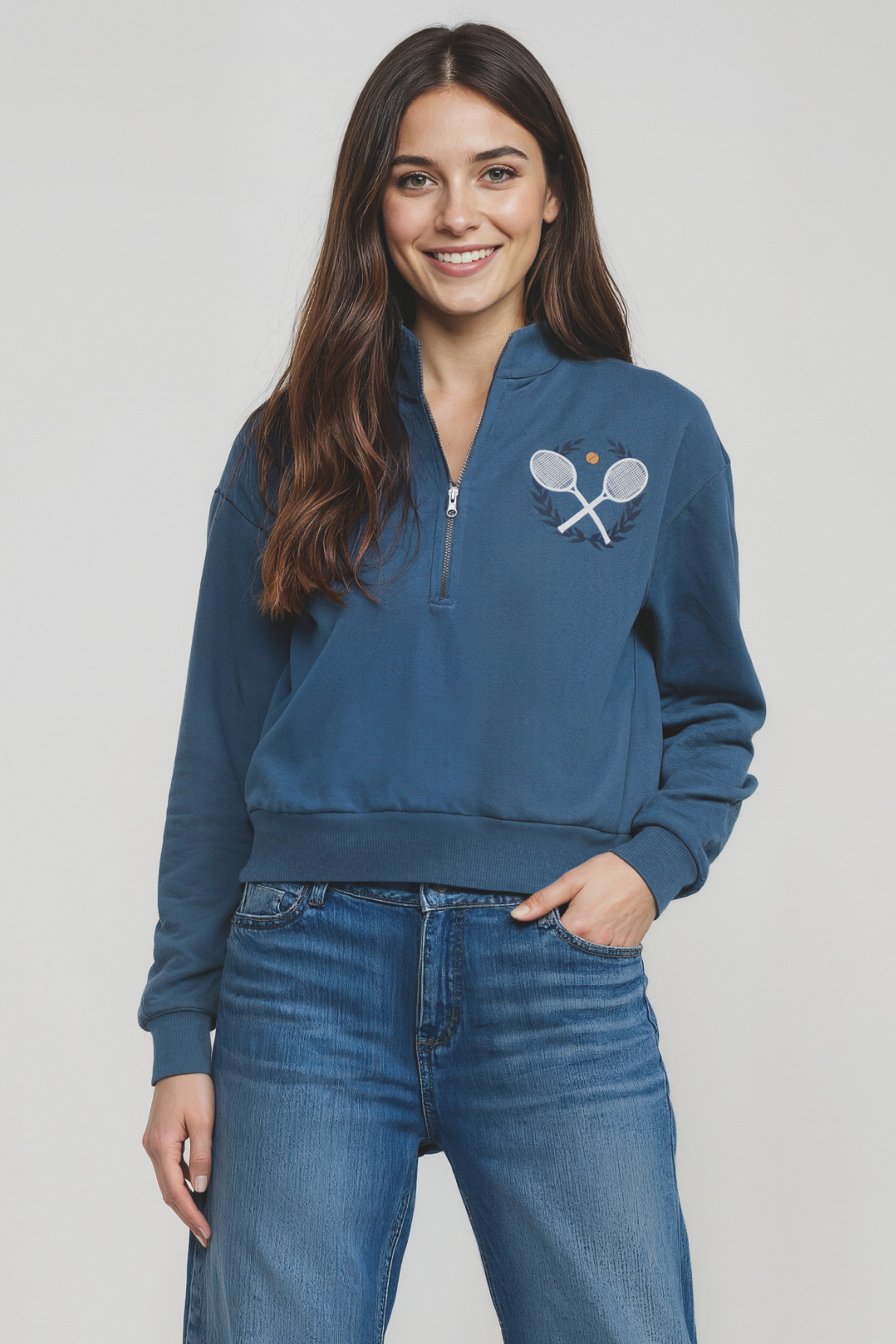 Woman wearing a blue 1/2 sweatshirt with a tennis racket design on a plain background