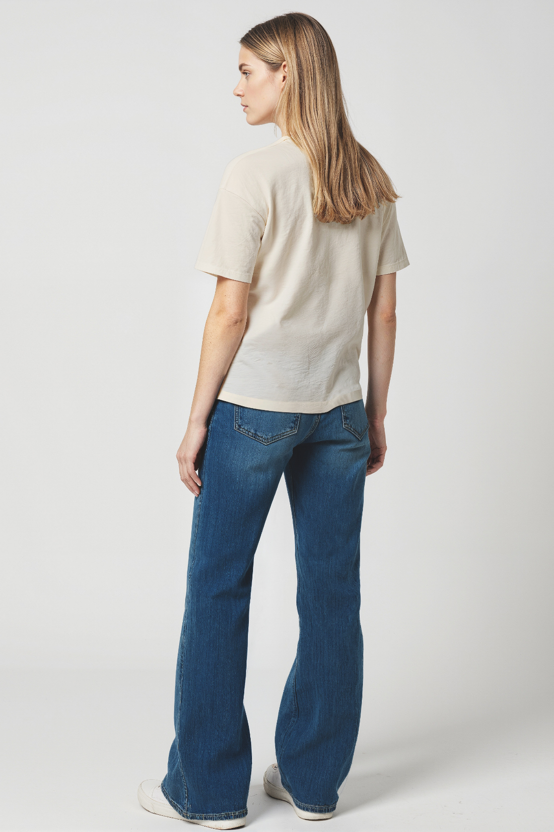 Back of Woman wearing a beige t-shirt and blue jeans on a white background