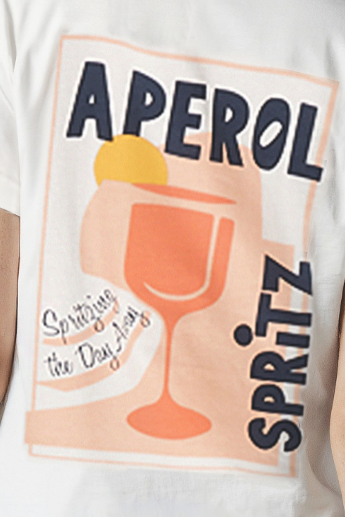 Close up of white T-shirt with "APEROL SPRITZ, Spritzing the Day Away" text and cocktail glass graphic design on a white background