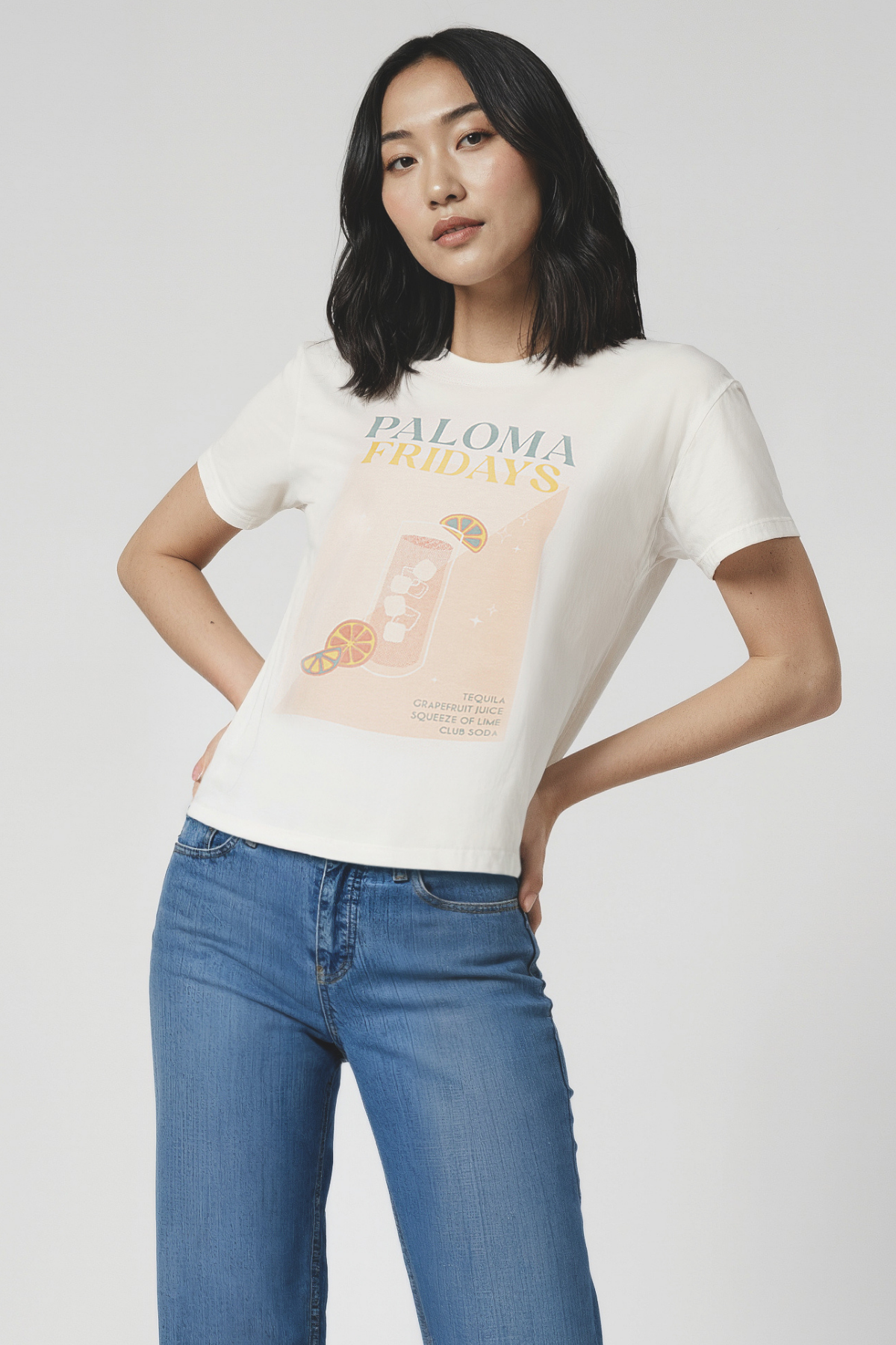Woman wearing a white t-shirt with a graphic design and blue jeans on a plain background