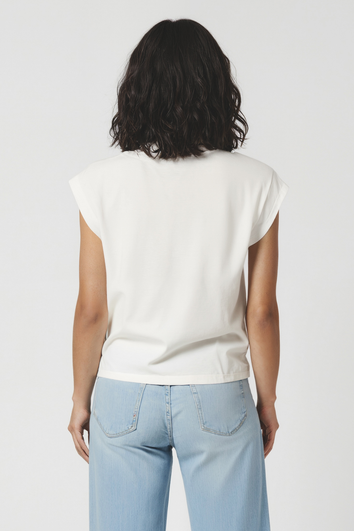 Back view of woman wearing a white t-shirt and light blue jeans on a plain background