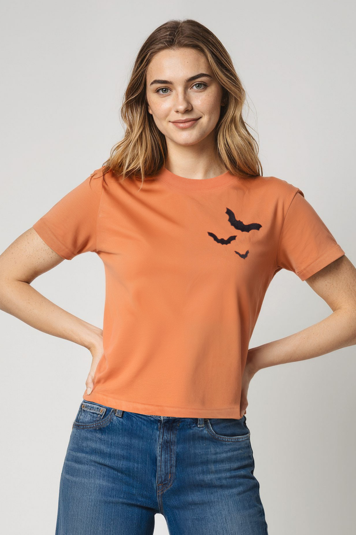 Woman wearing an orange t-shirt with a 3 black bats design on a plain background.