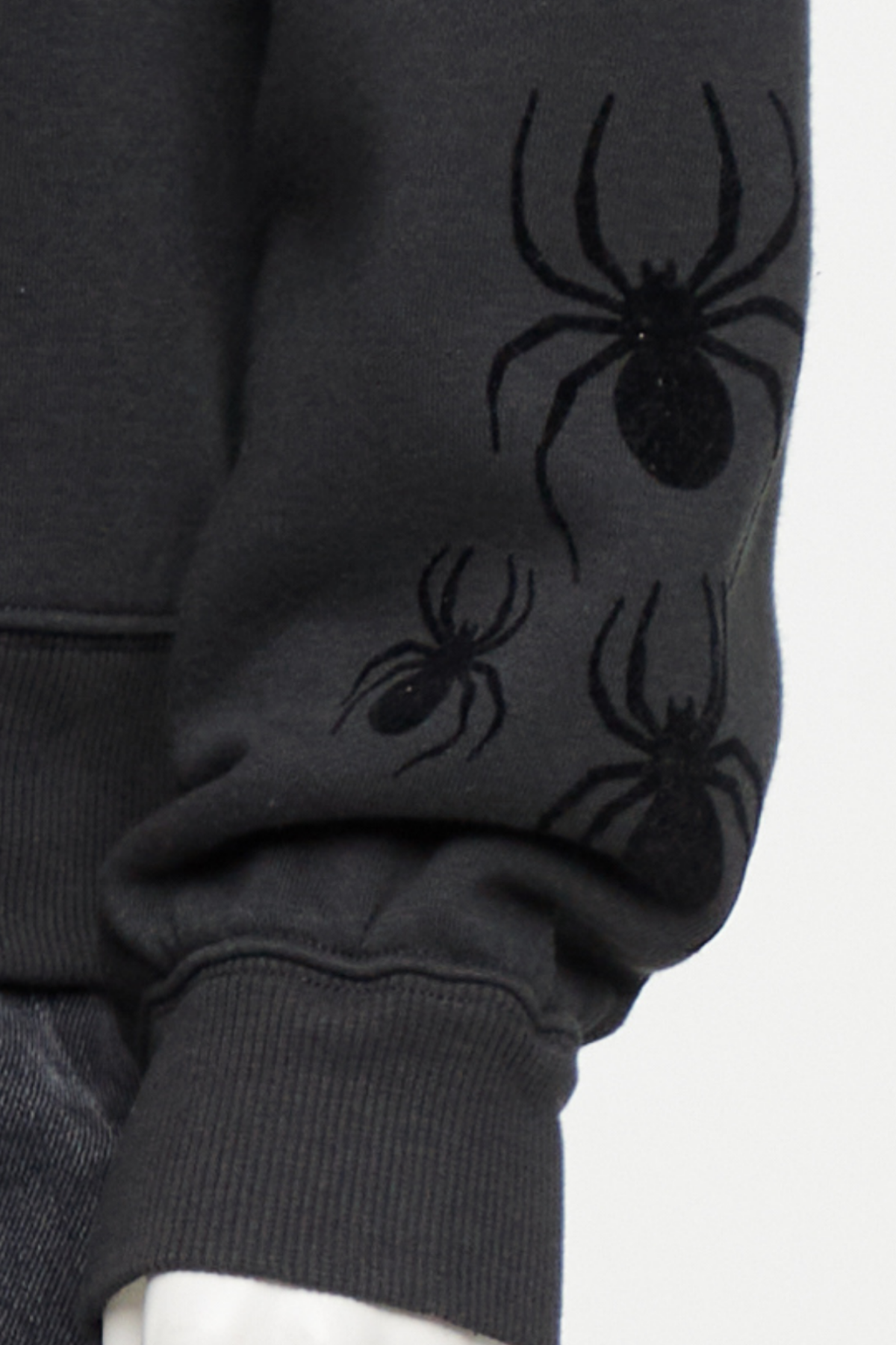 Close up of black hoodie with spider designs on lower left sleeve cuff on a white background