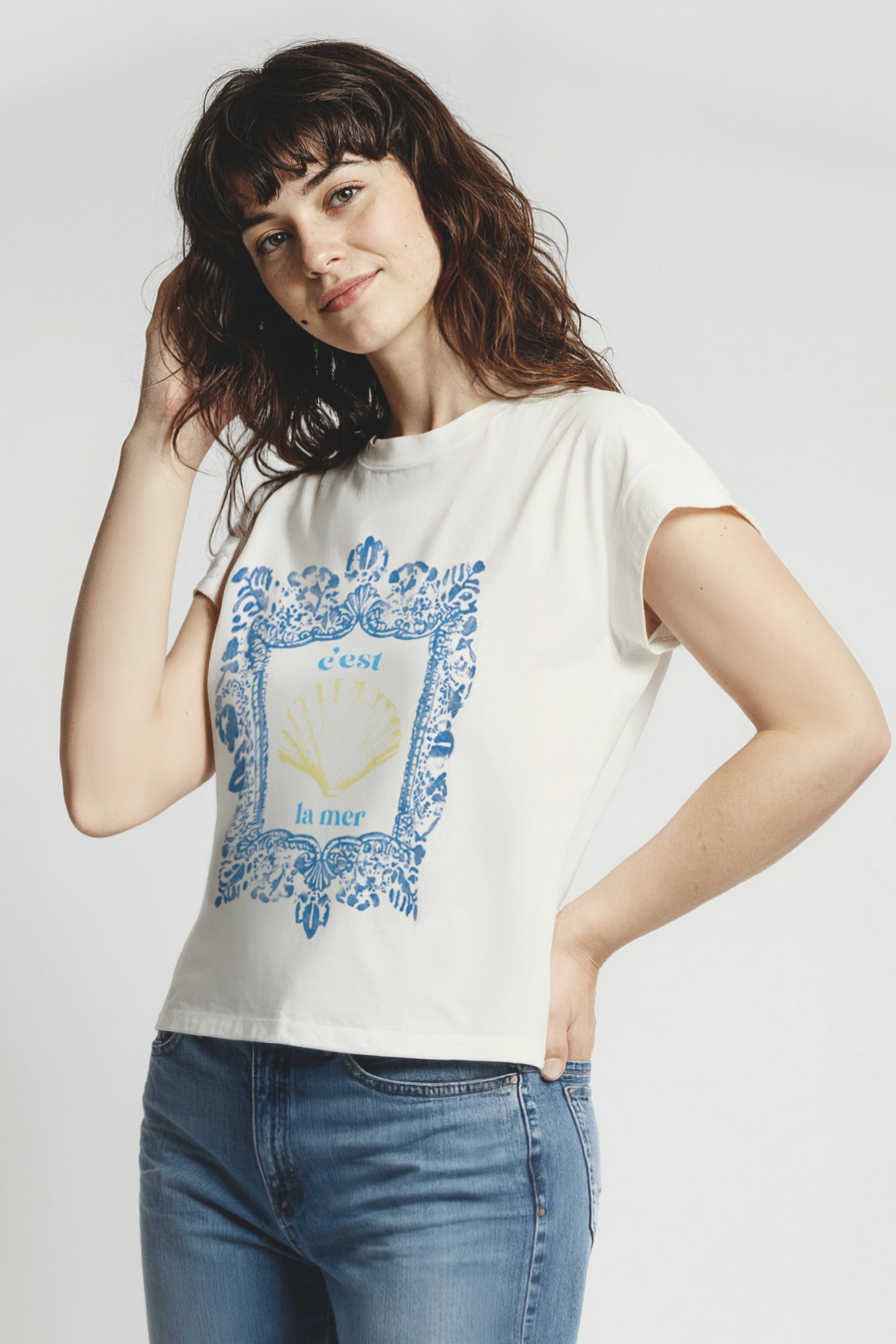 Woman wearing white t-shirt with blue frame graphic design featuring a yellow shell and &