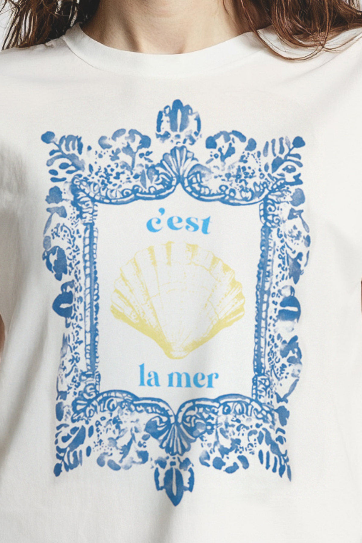 Close up of woman wearing white t-shirt with blue frame graphic design featuring a yellow shell and &