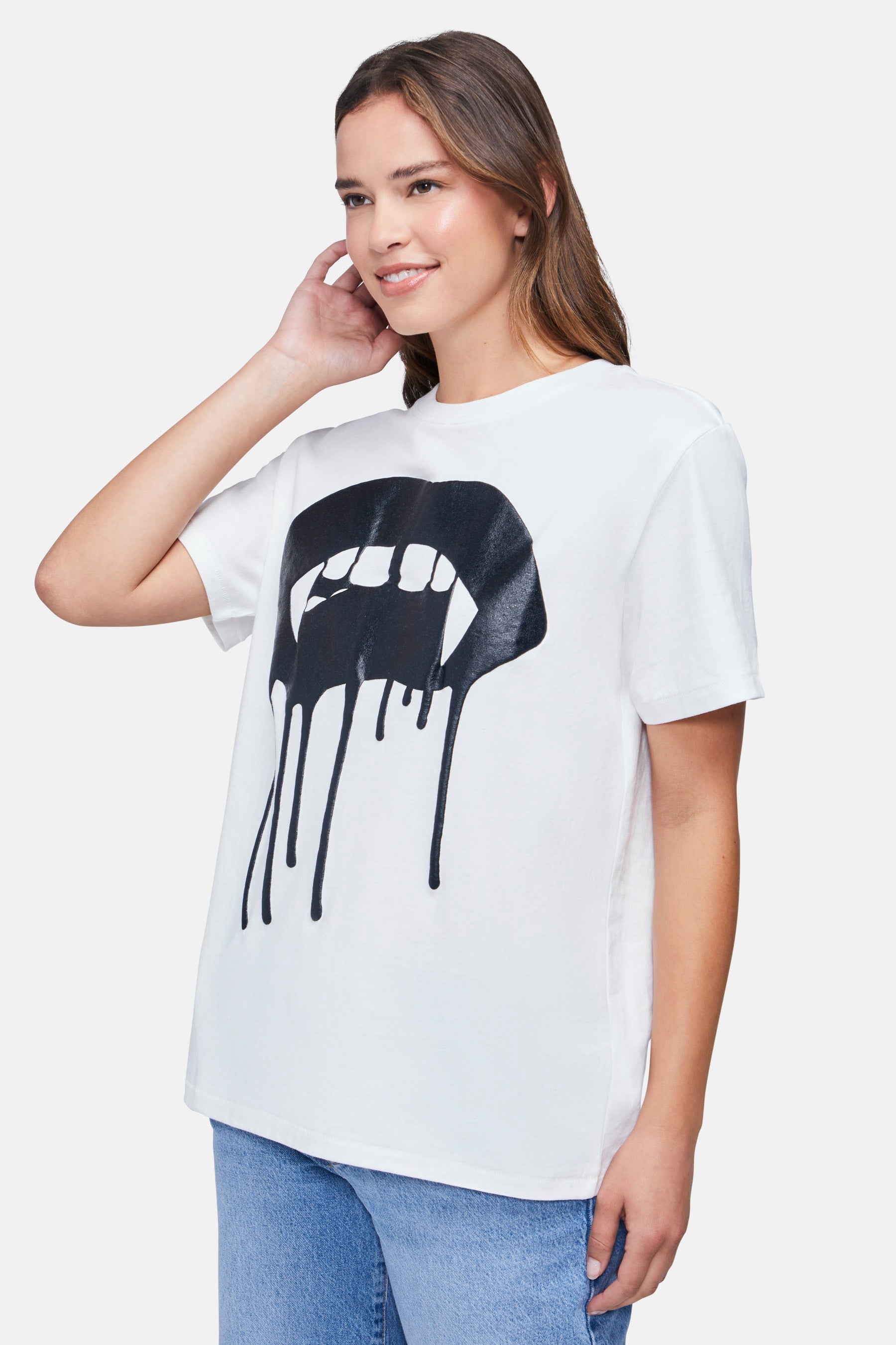 A woman wearing a white t-shirt with the black large vampire lips with drips graphic paired with denim jeans.