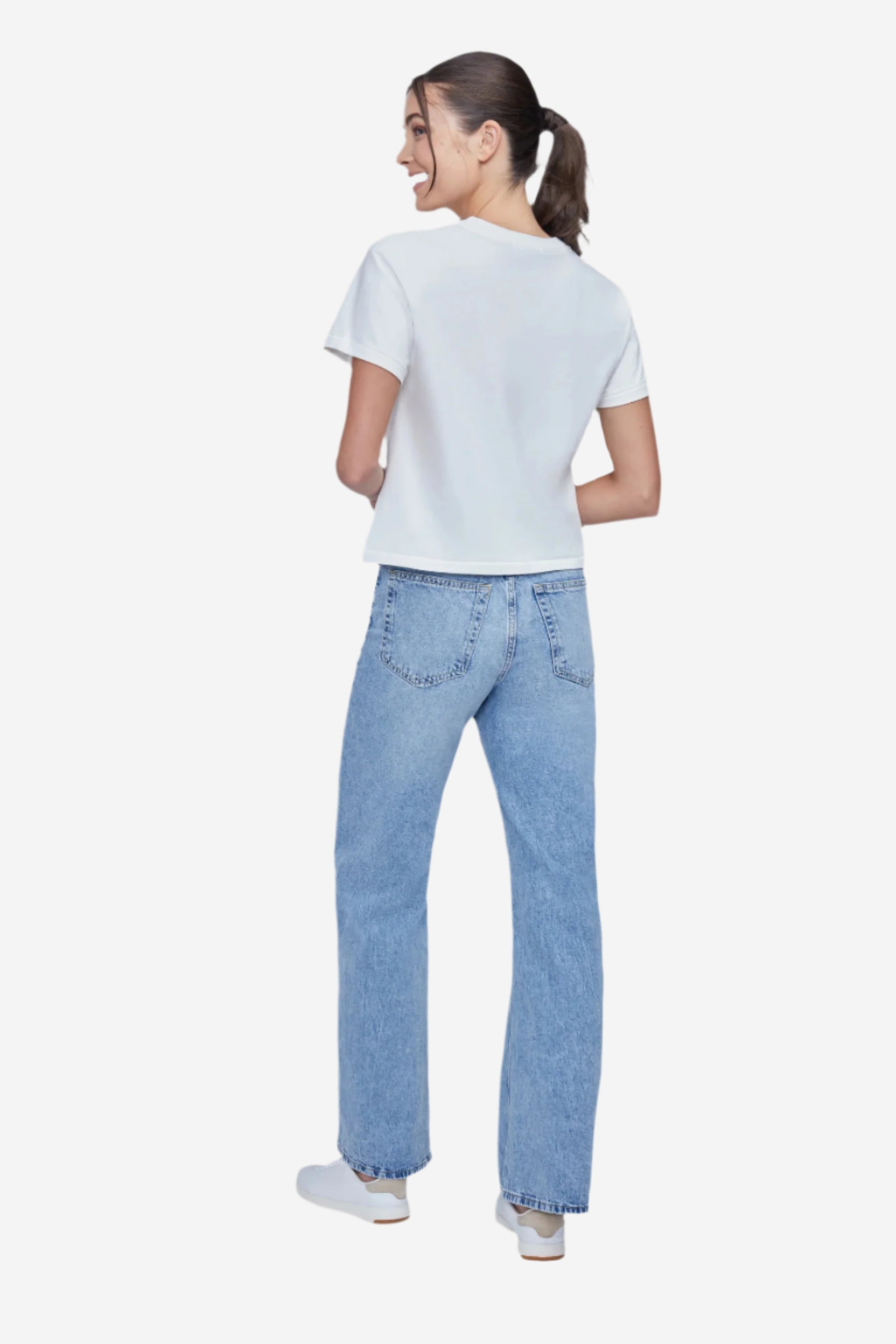 Back of woman wearing a white t-shirt and blue jeans on a plain background.