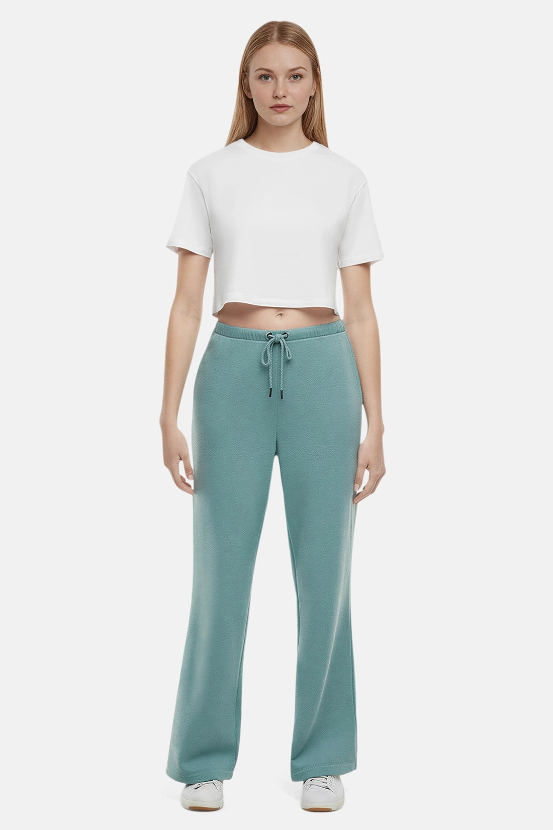 Woman wearing a white cropped t-shirt and teal wide-leg drawstring sweatpants on a white background