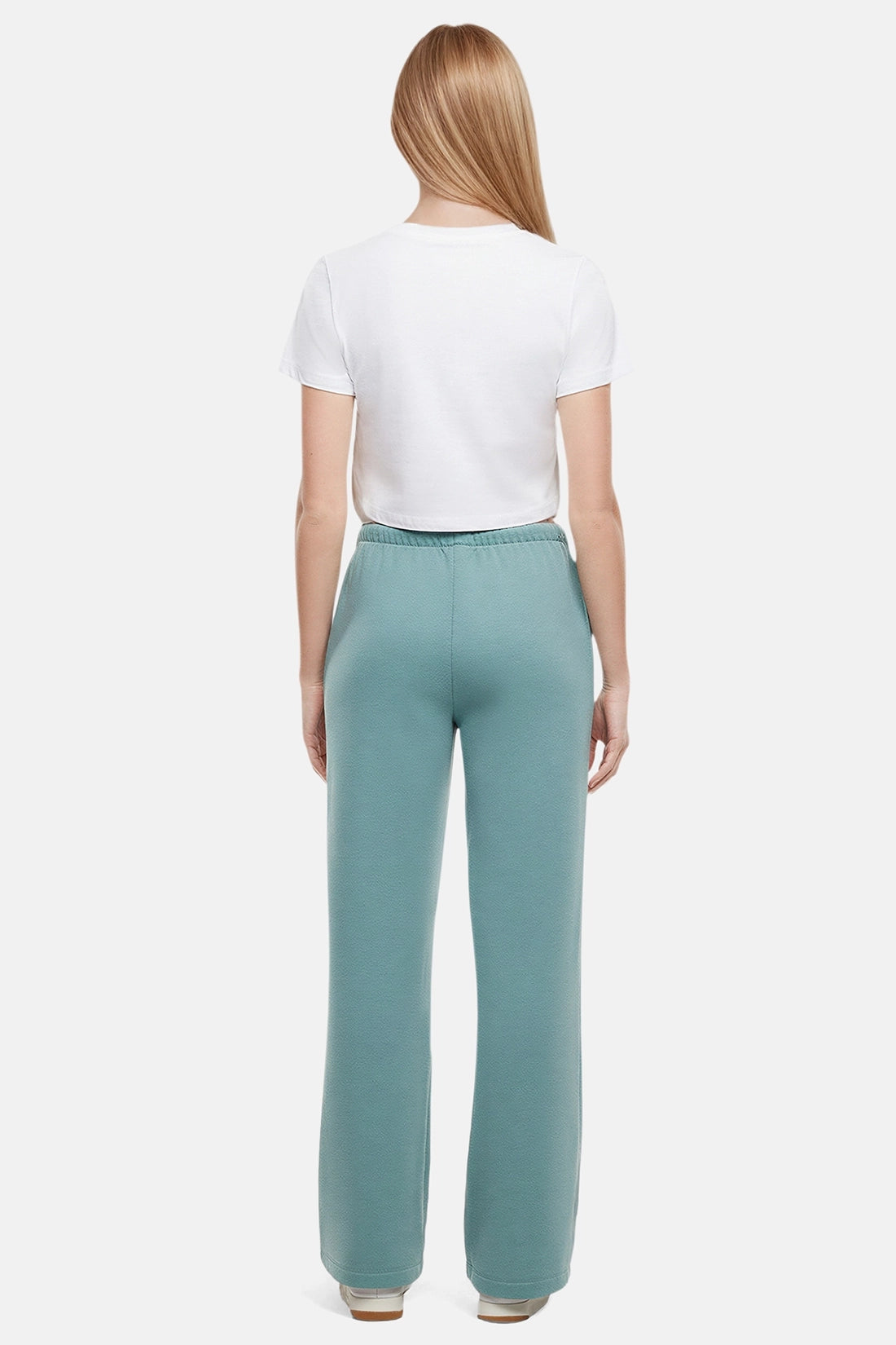 Back of woman wearing a white cropped t-shirt and teal wide-leg drawstring sweatpants on a white background