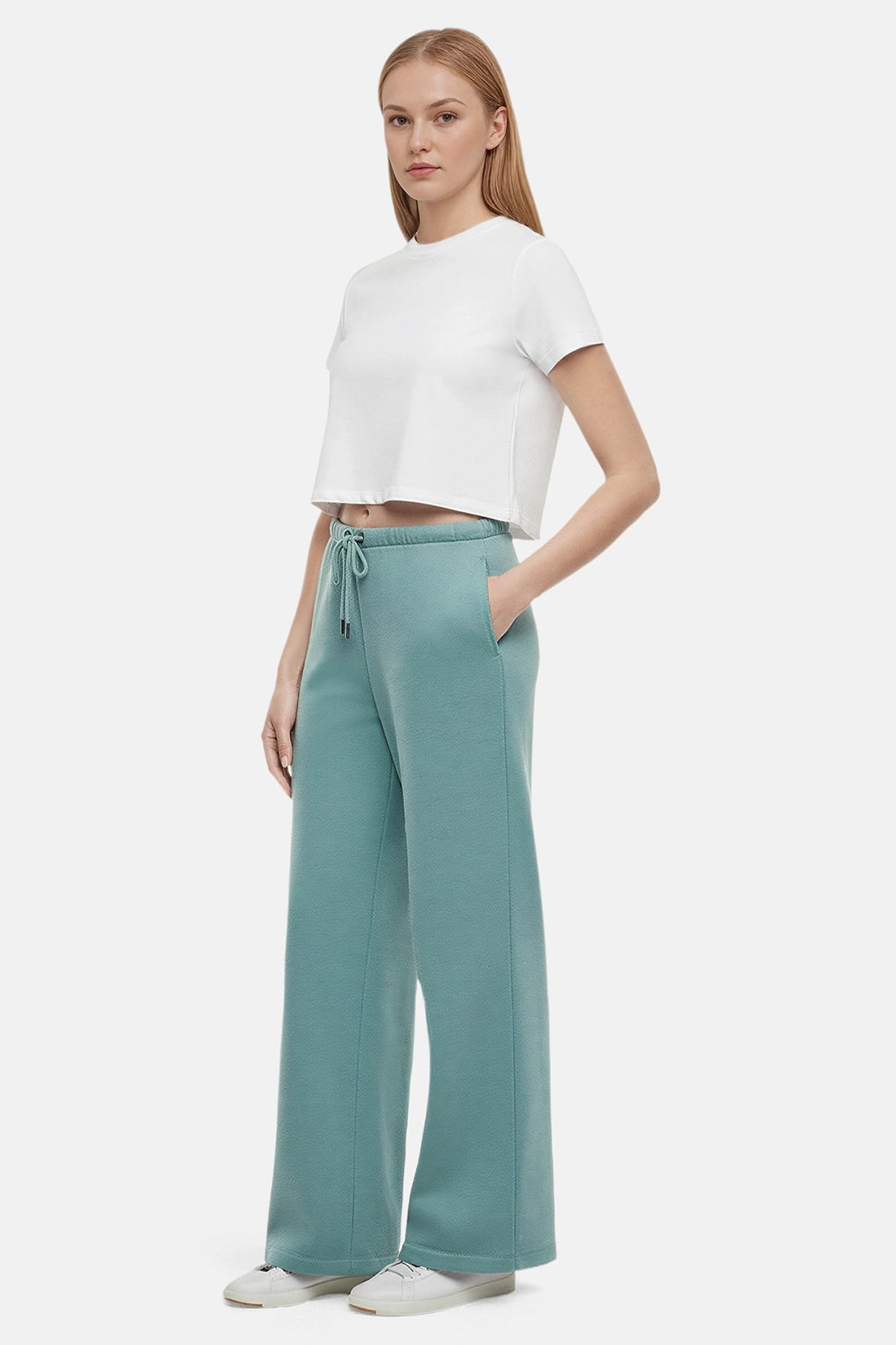 Woman wearing a white cropped t-shirt and teal wide-leg drawstring sweatpants on a white background