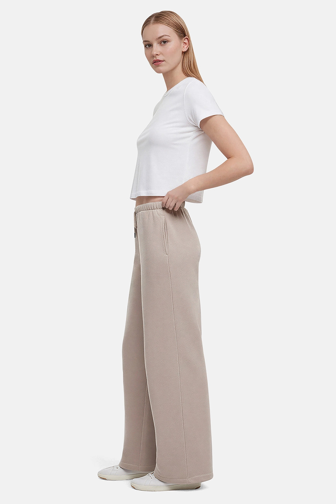 Woman wearing a white cropped t-shirt and beige wide-leg drawstring sweatpants on a white background