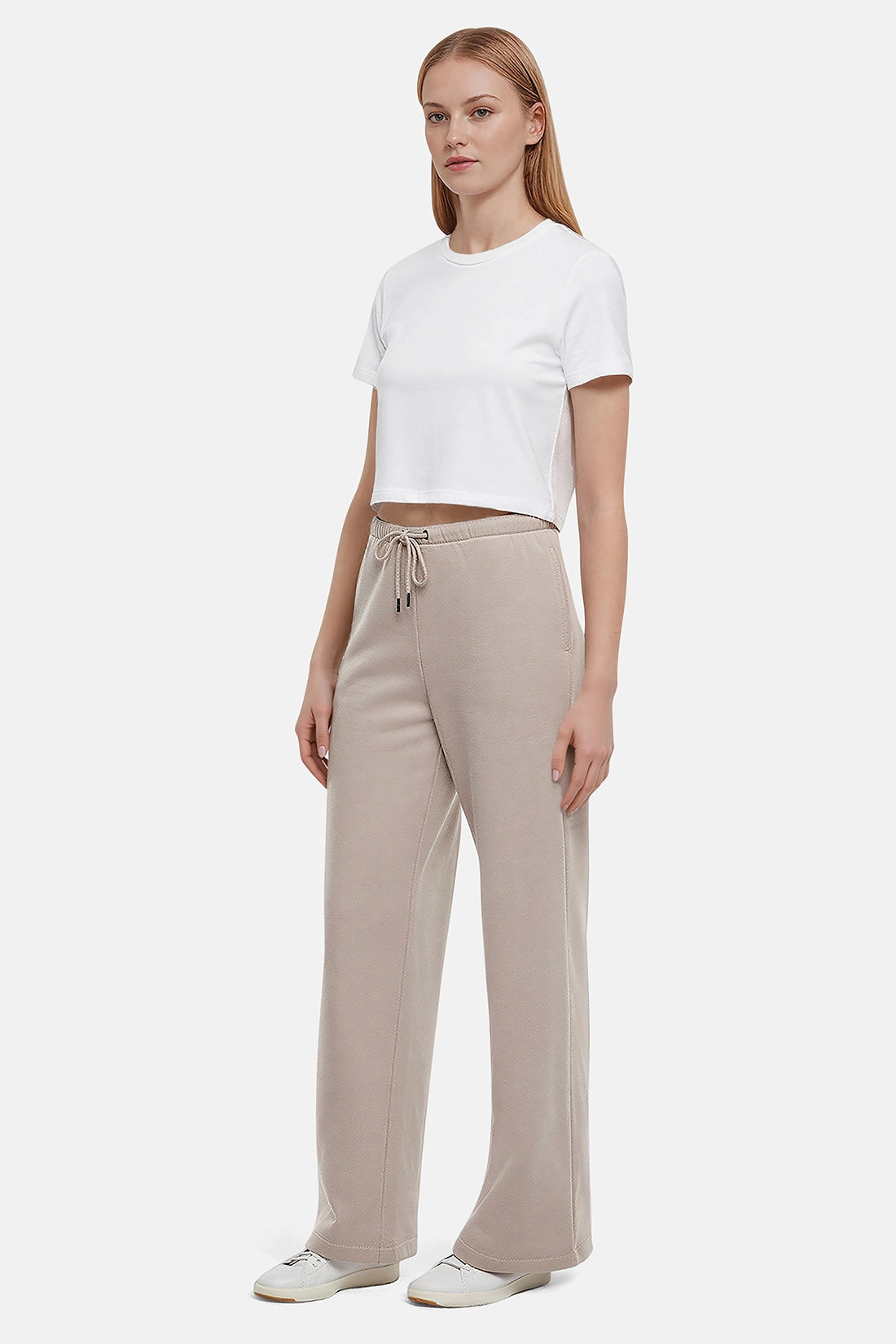 Woman wearing a white cropped t-shirt and beige wide-leg drawstring sweatpants on a white background