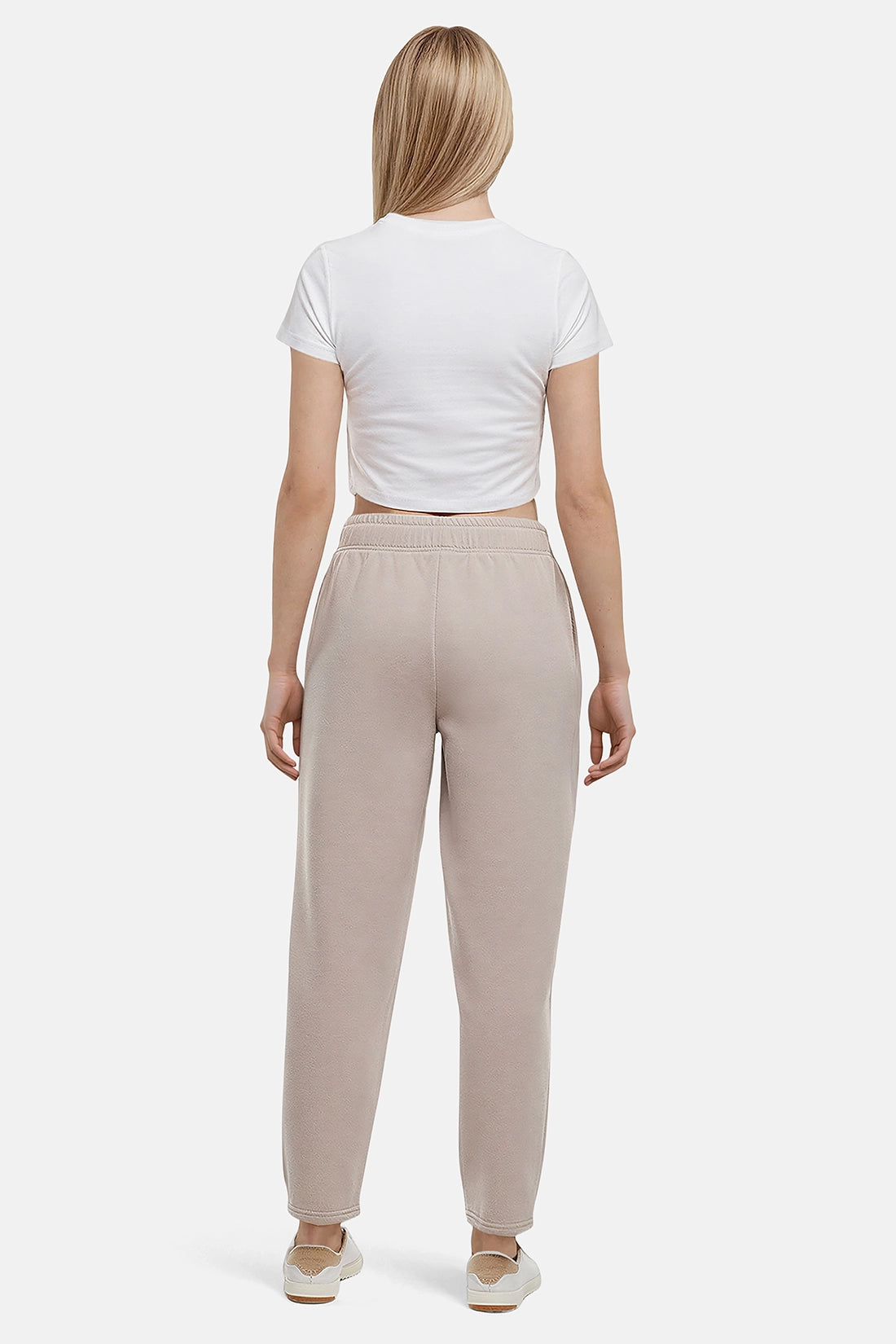 Back of woman wearing a white t-shirt and beige tapered leg pants on a white background