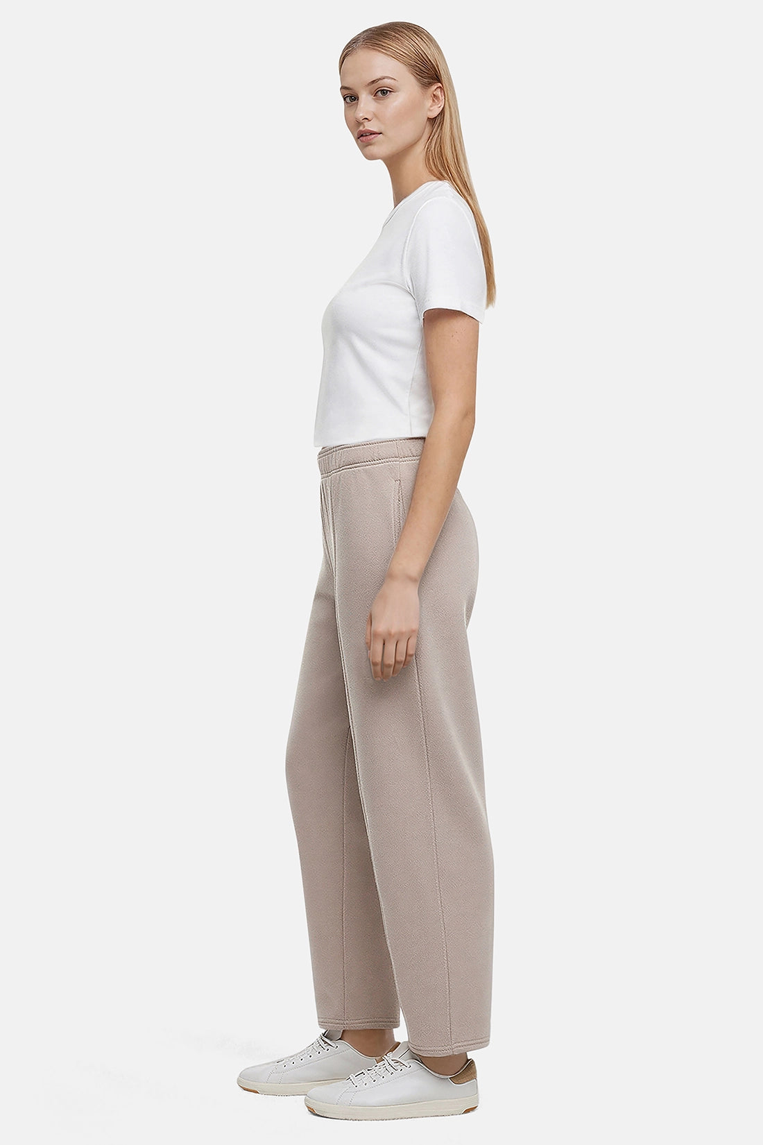 Side view of woman wearing a white t-shirt and beige tapered leg pants on a white background