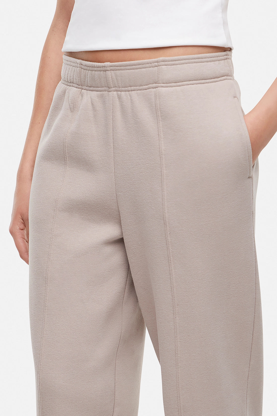 Close up of front of woman wearing a white t-shirt and beige tapered leg pants on a white background