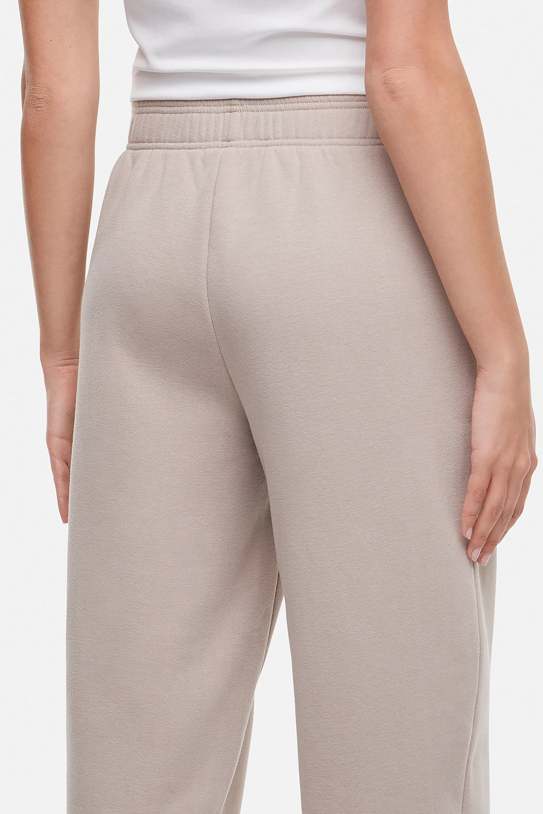 Close up of back of woman wearing a white t-shirt and beige tapered leg pants on a white background