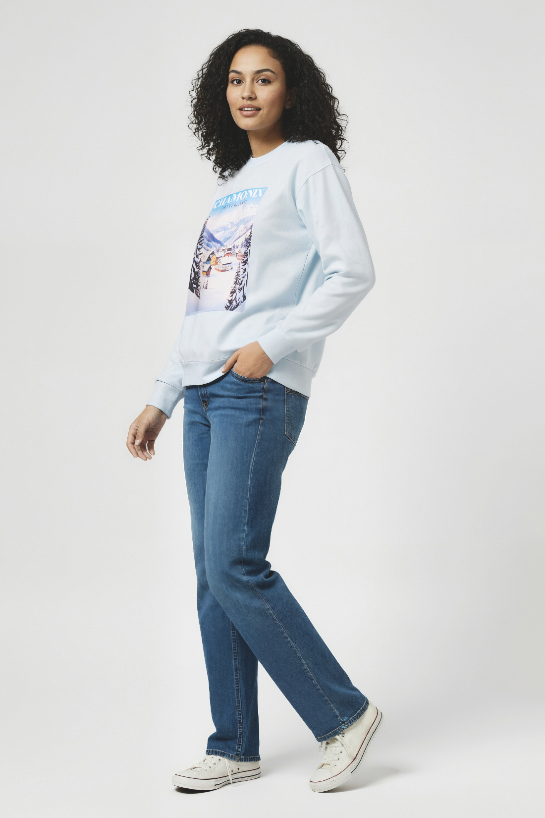 Woman wearing a light blue sweatshirt with a mountain graphic and &