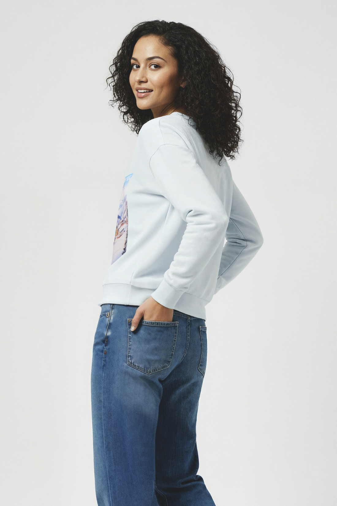 Woman wearing a light blue sweatshirt and blue jeans on a white background