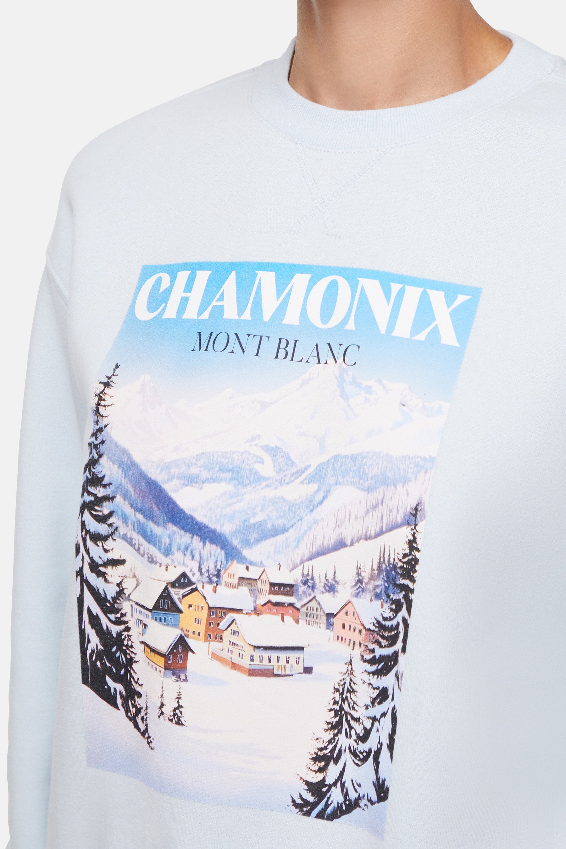 Close up of light blue sweatshirt with a mountain village graphic and &