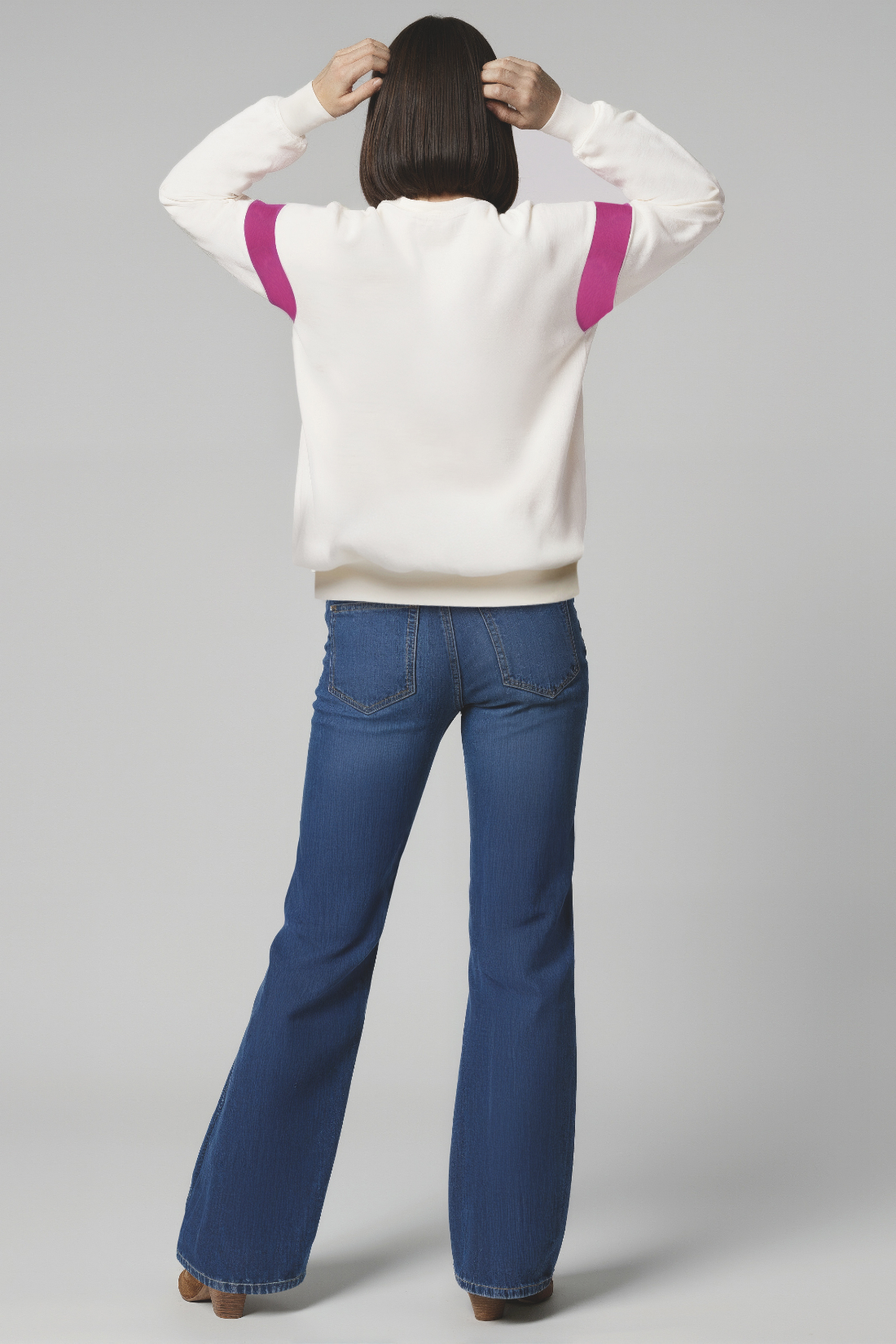 Back of woman wearing a white sweater with purple accents and blue jeans on a white background