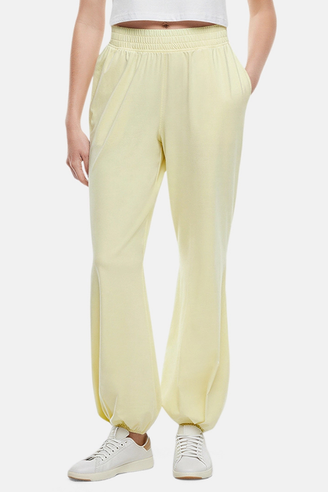 Close up front view of woman wearing yellow pants, white tee and white sneakers on a white background.
