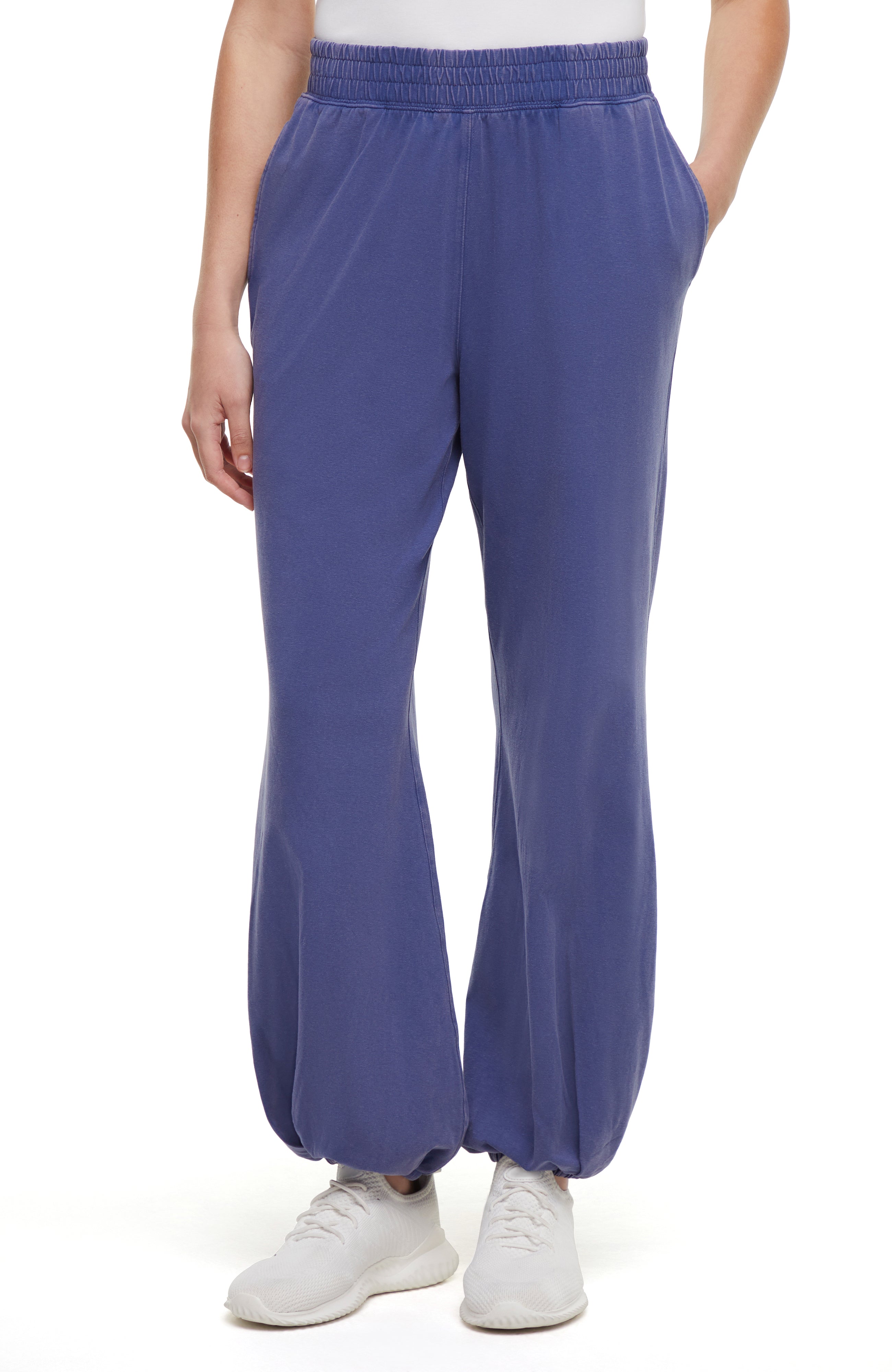 Front view of woman wearing blue pants and white sneakers on a white background.