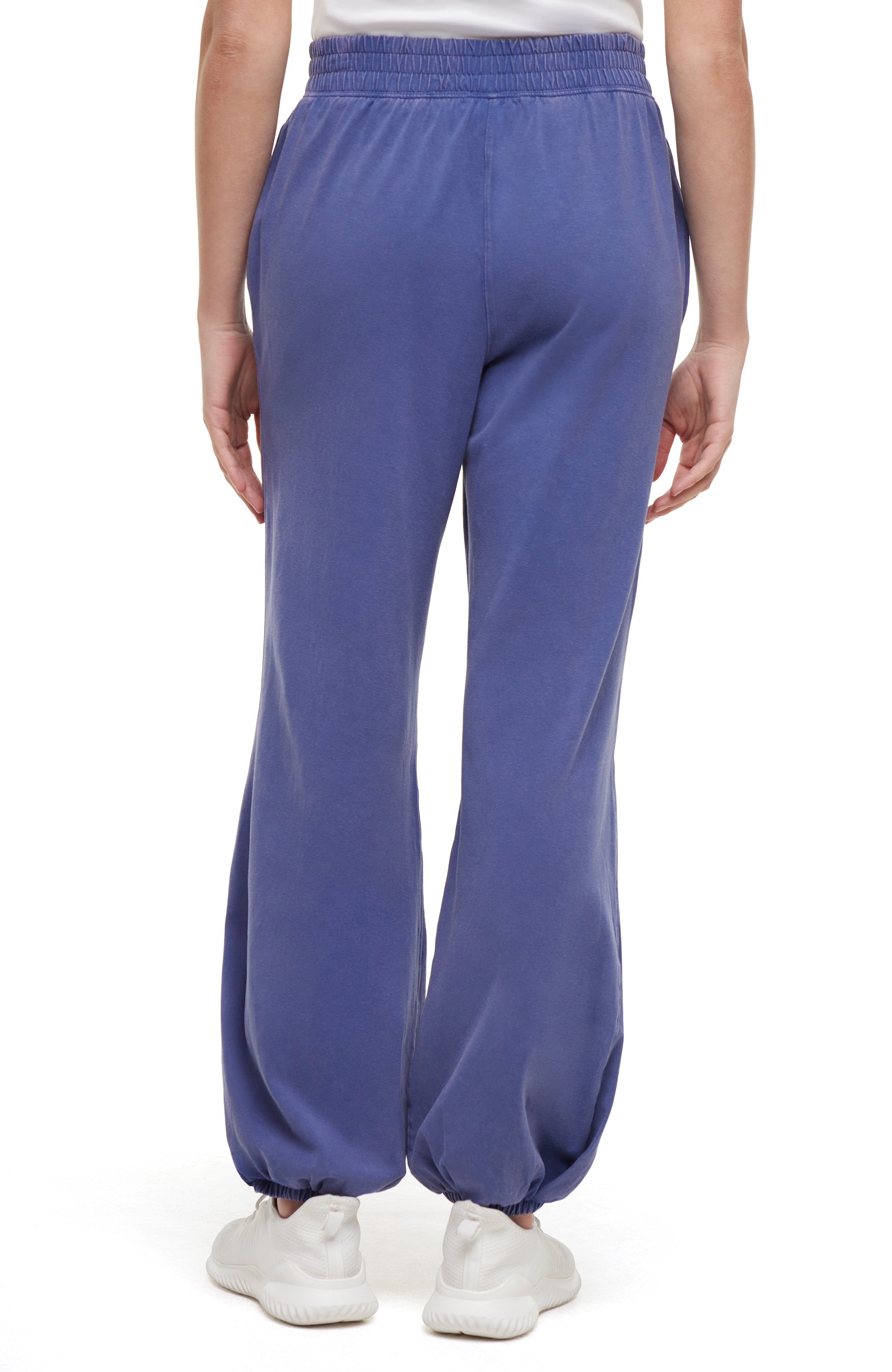 Back view of woman wearing blue pants and white sneakers on a white background.