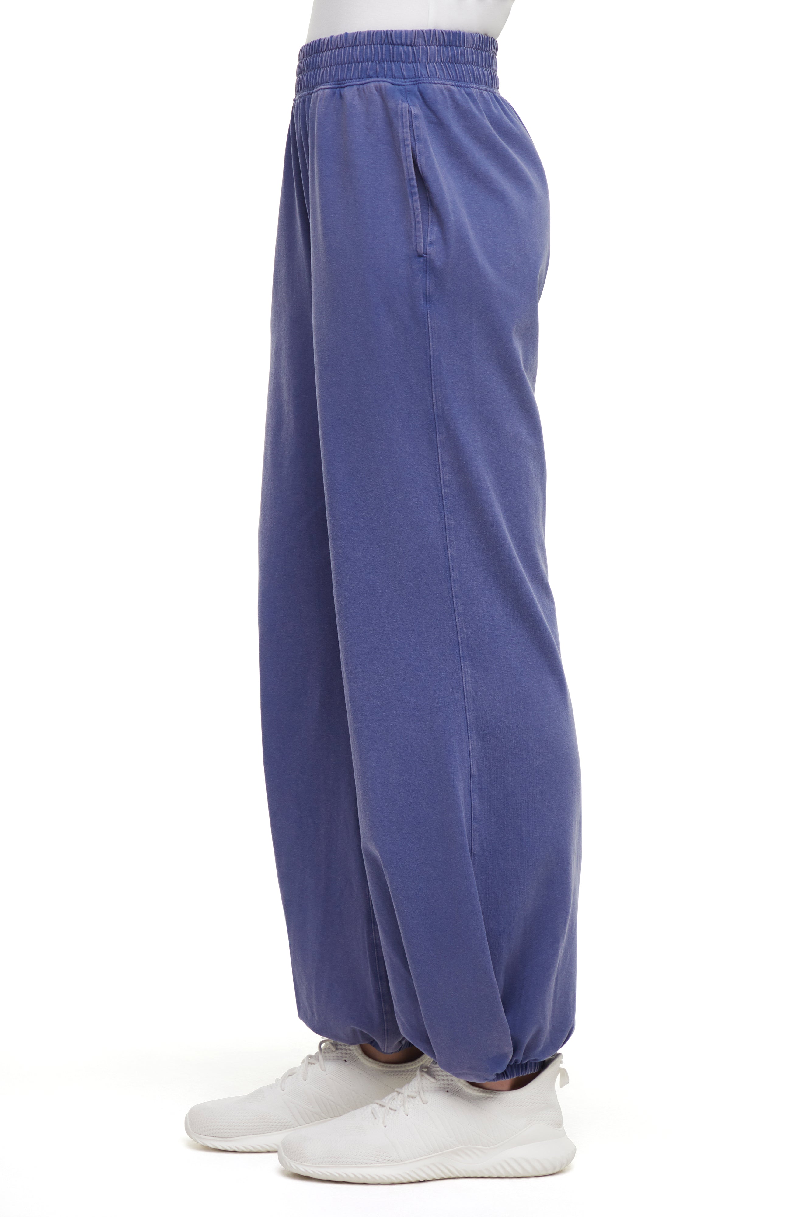 Side view of woman wearing blue pants and white sneakers on a white background.