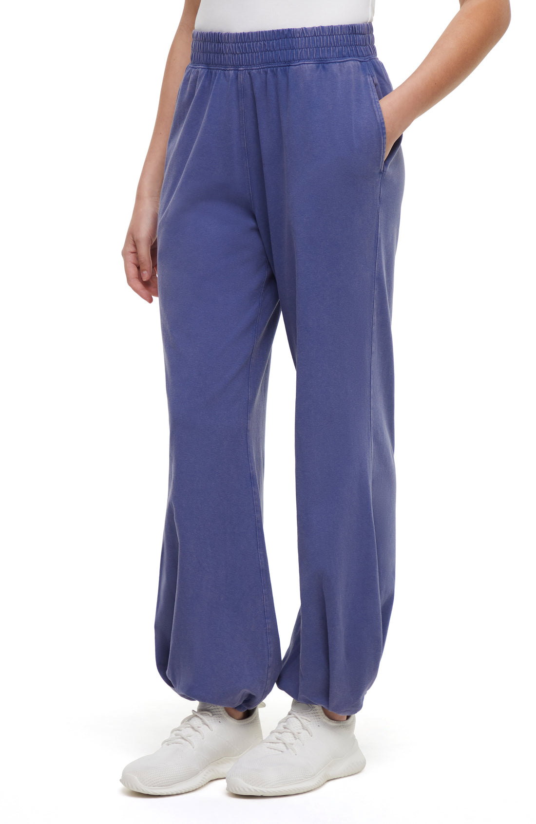 Front view of woman wearing blue pants and white sneakers on a white background.