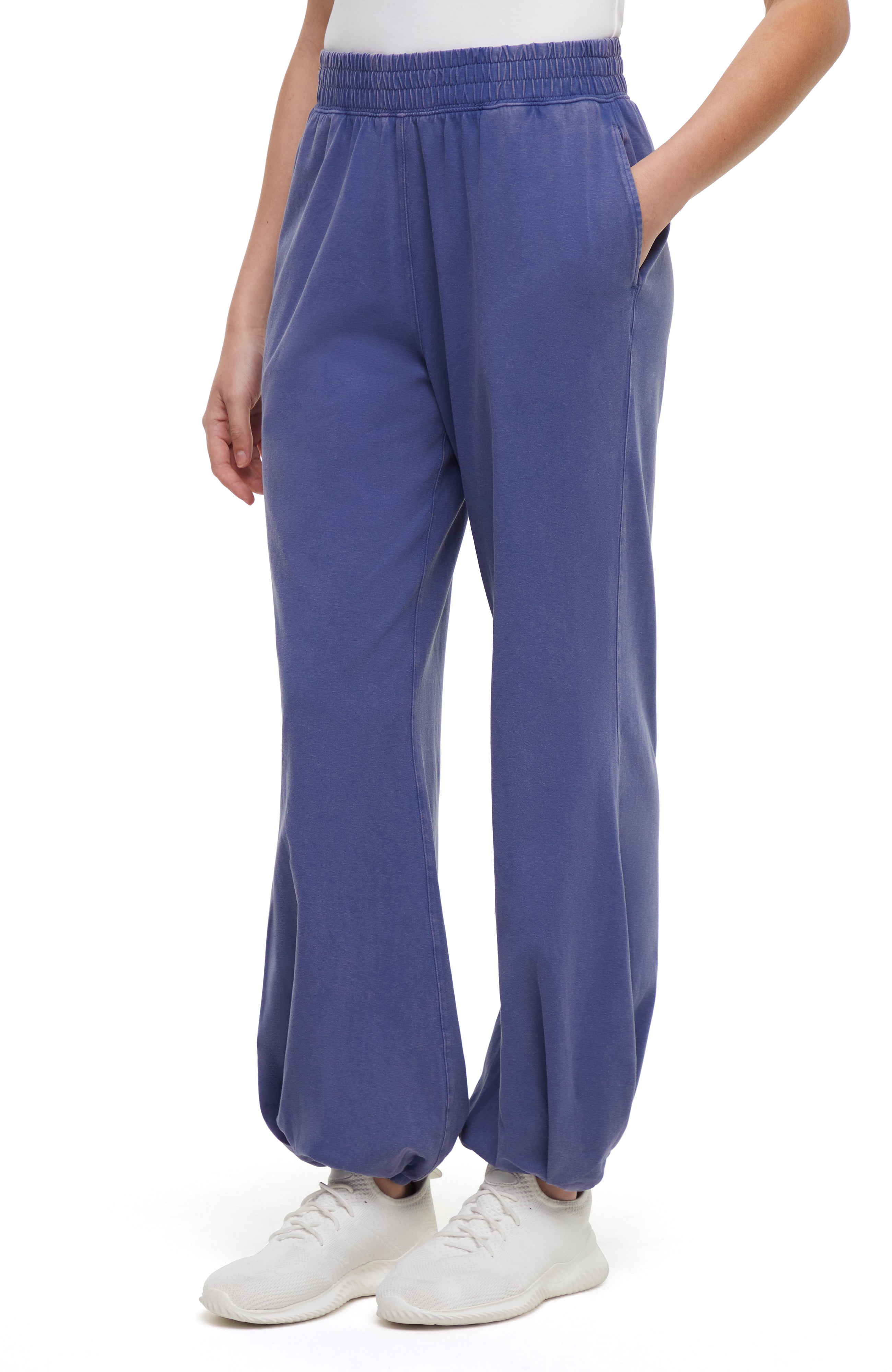 Front view of woman wearing blue pants and white sneakers on a white background.