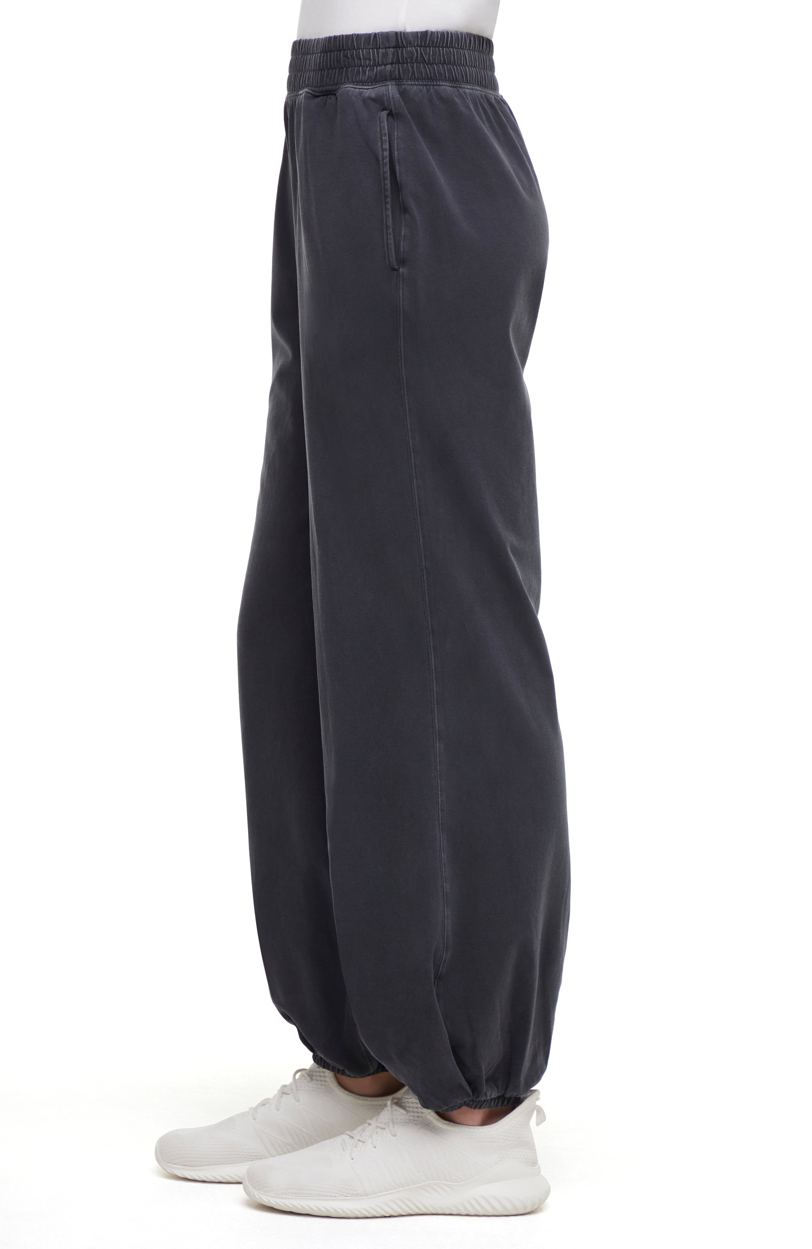 Side view of woman wearing dark gray pants and white sneakers on a white background.