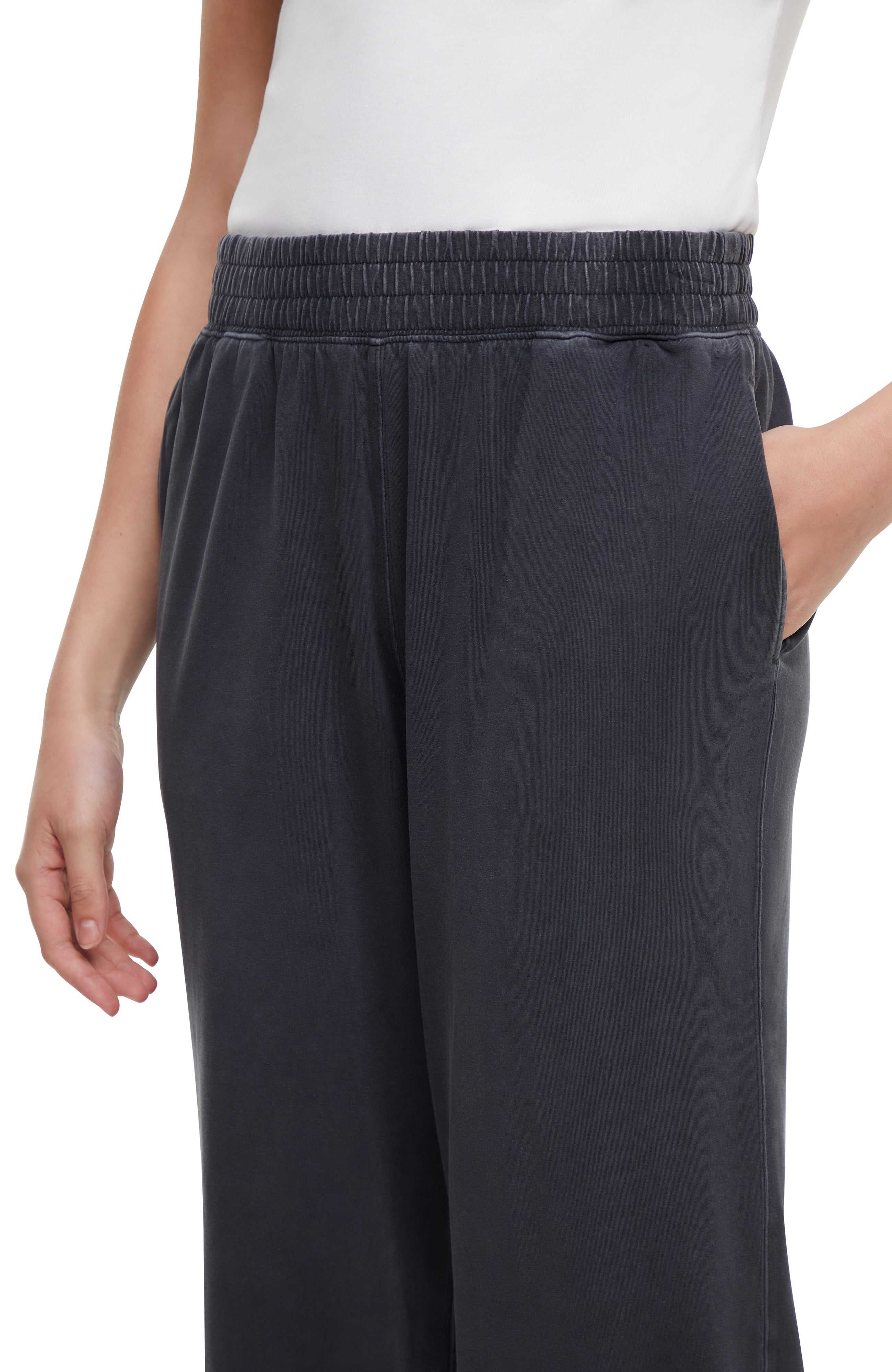 Close up front view of woman wearing dark gray pants and white sneakers on a white background.