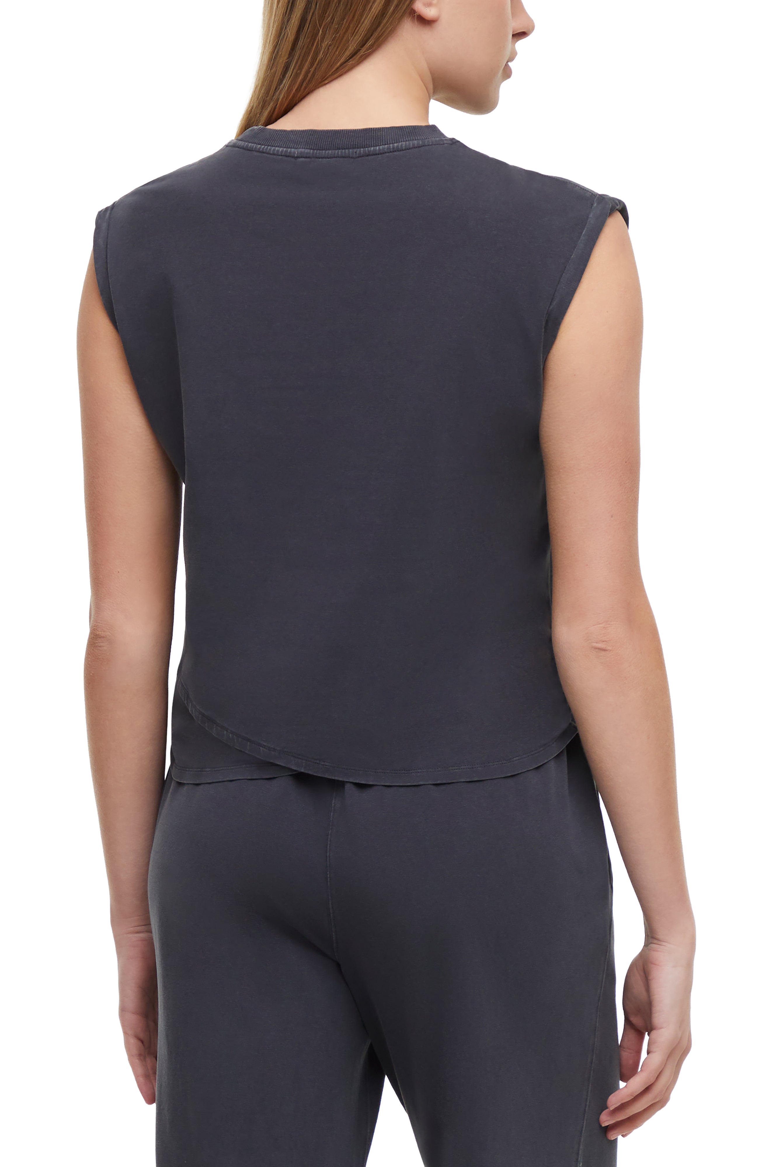 Back view of woman wearing a dark gray sleeveless asymmetrical top and pants on a white background.