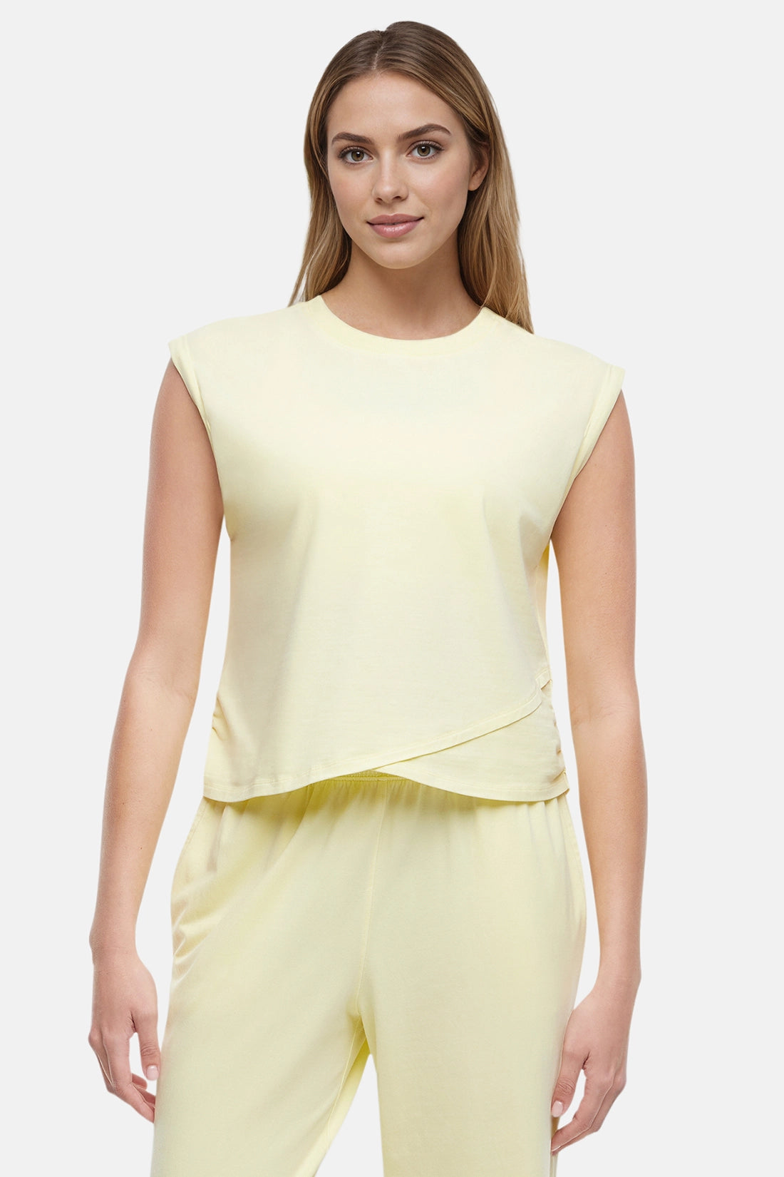 Front view of woman wearing a light-yellow sleeveless asymmetrical top and pants on a white background.