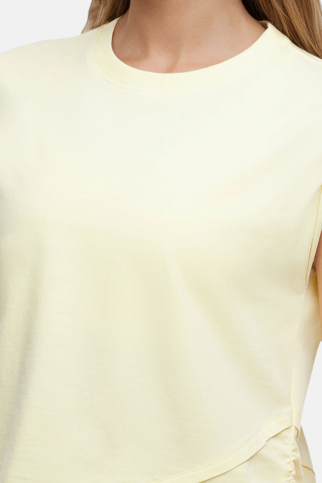 Front close up view of woman wearing a light-yellow sleeveless asymmetrical top and pants on a white background.