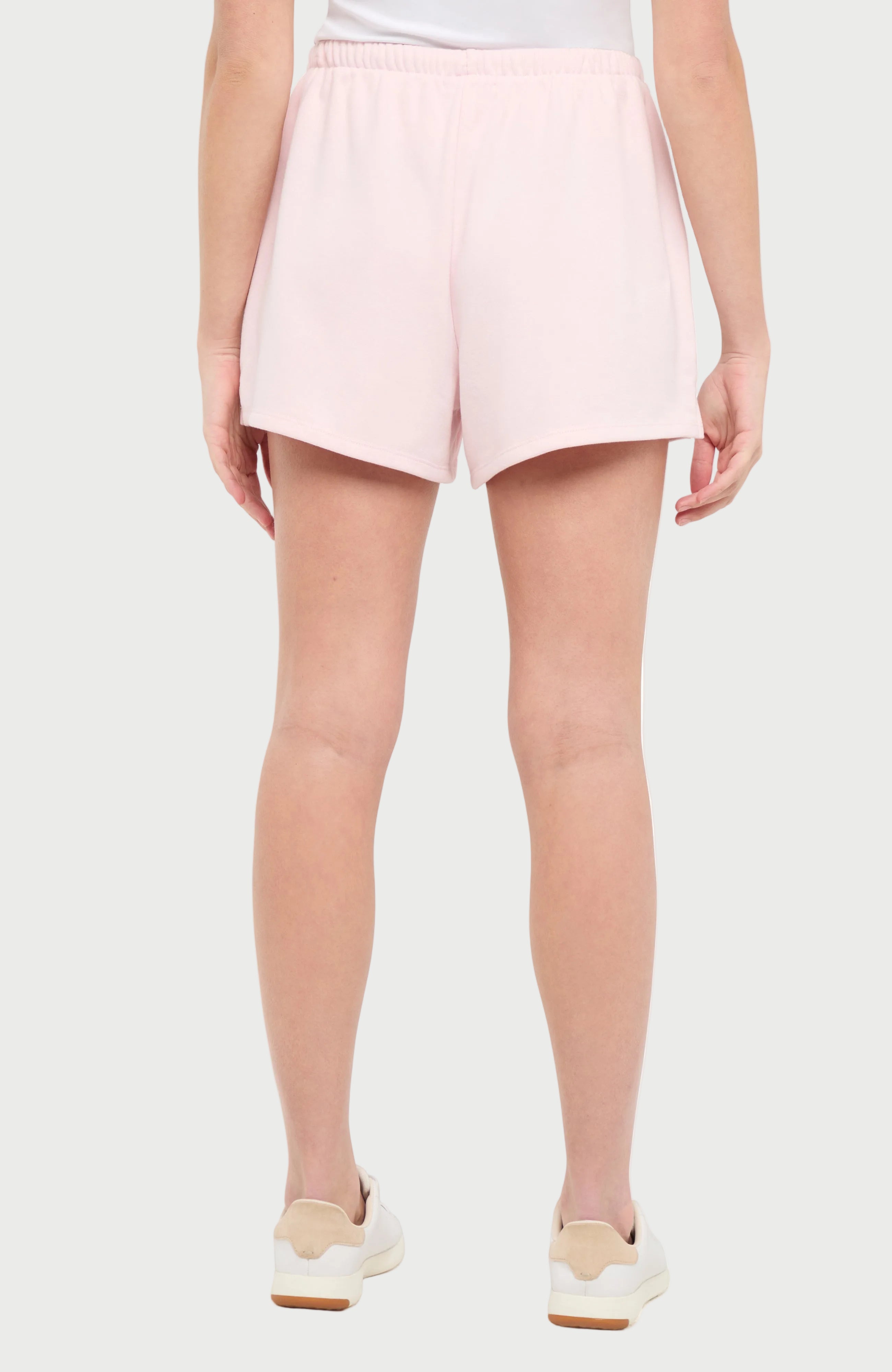 Back view of woman wearing light pink shorts on a white background.