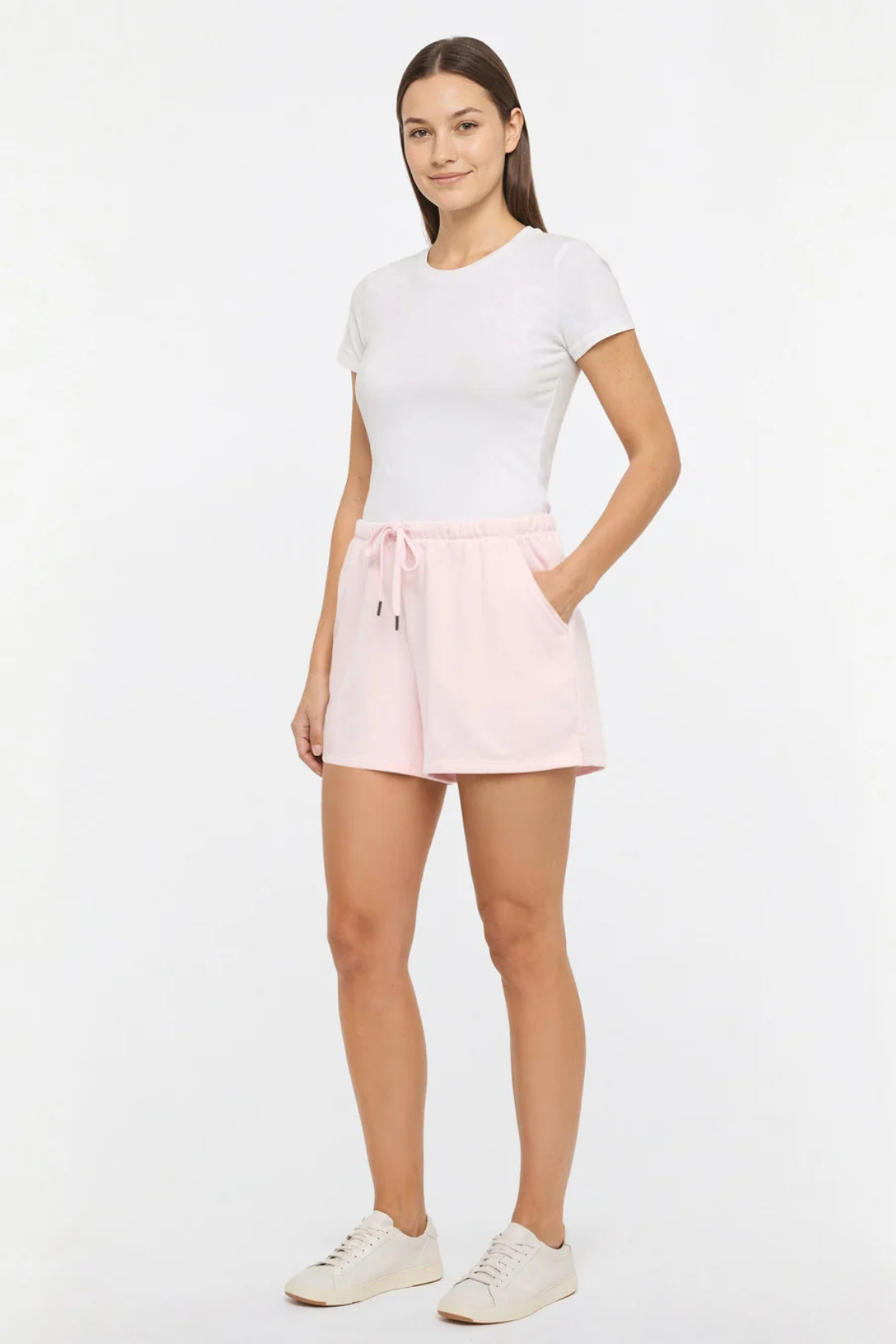 Front view of woman wearing light pink shorts and white tee on a white background.