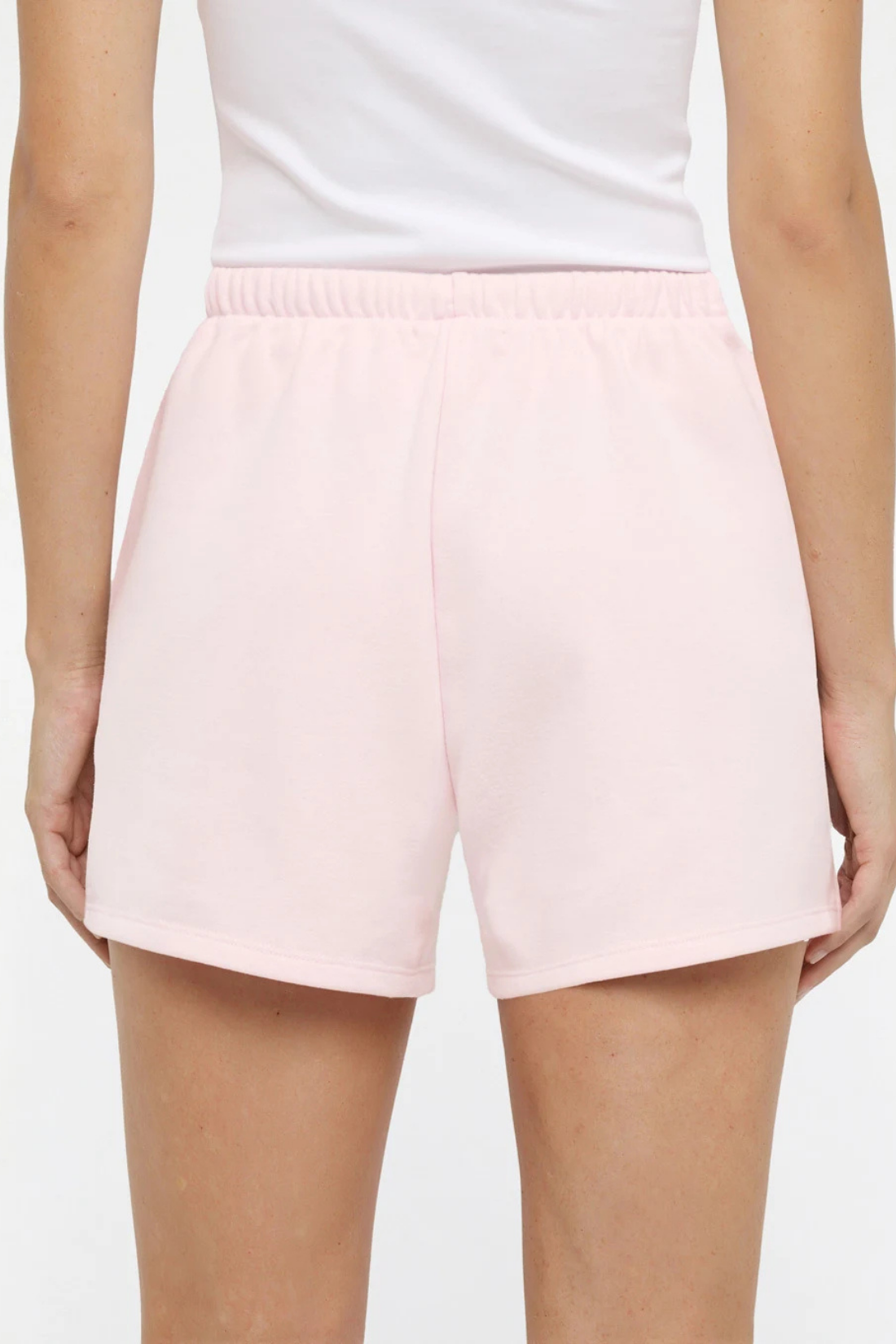Close up back view of woman wearing light pink shorts on a white background.