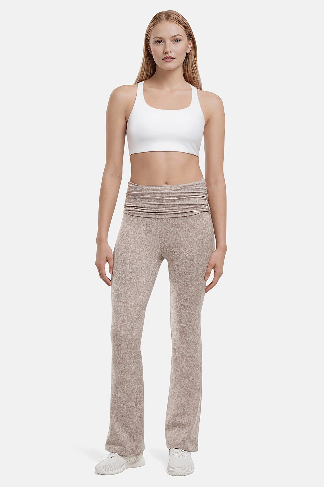 Woman wearing a white sports bra and beige yoga pants on a white background