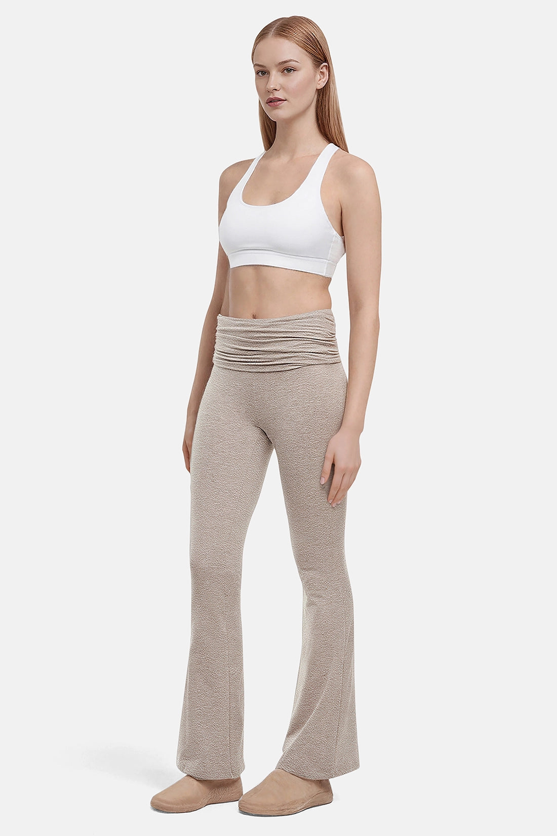 Side view of woman wearing a white sports bra and beige yoga pants on a white background