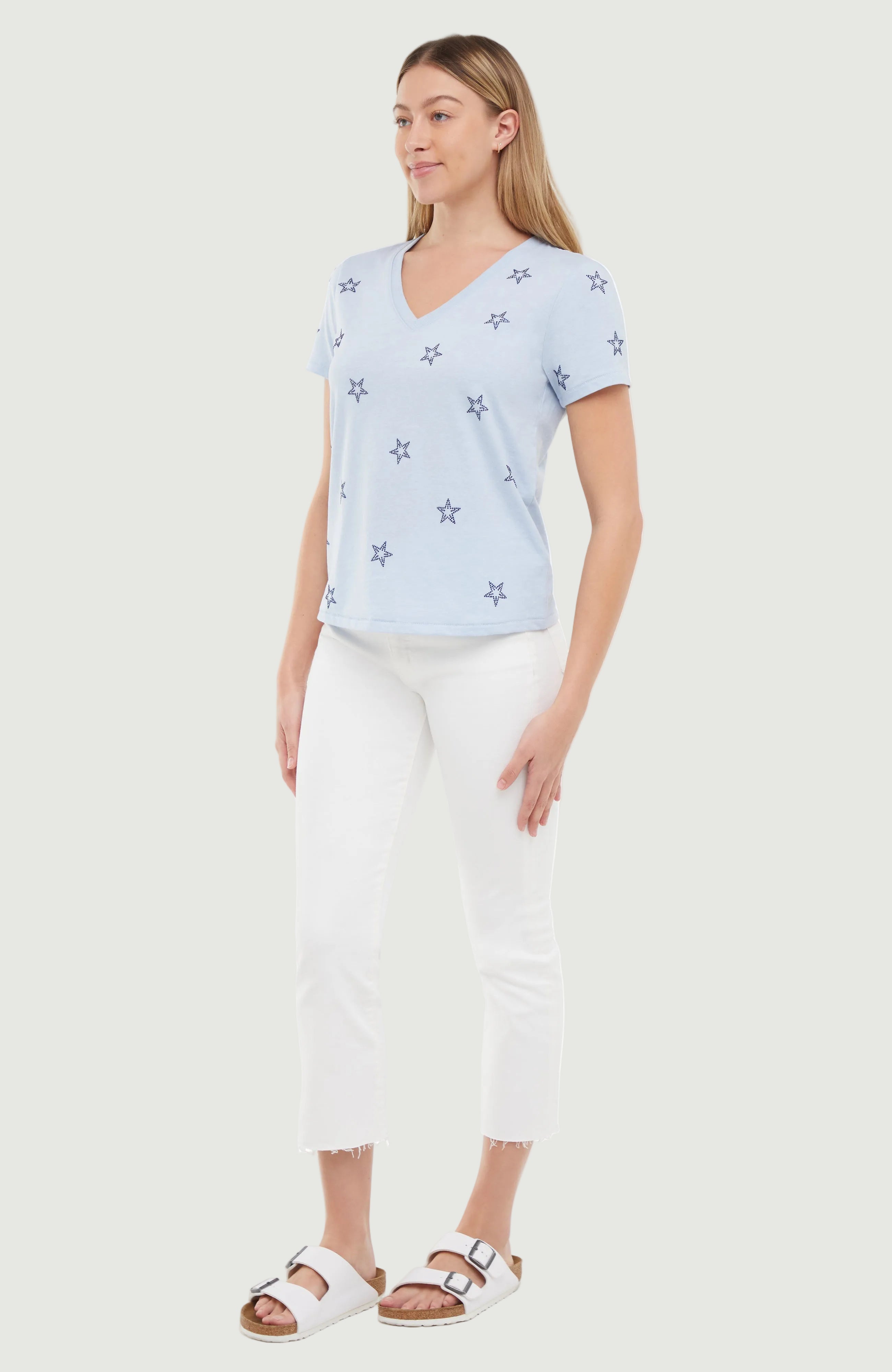 Side view of woman wearing a light blue t-shirt with blue rhinestone star patterns on a white background