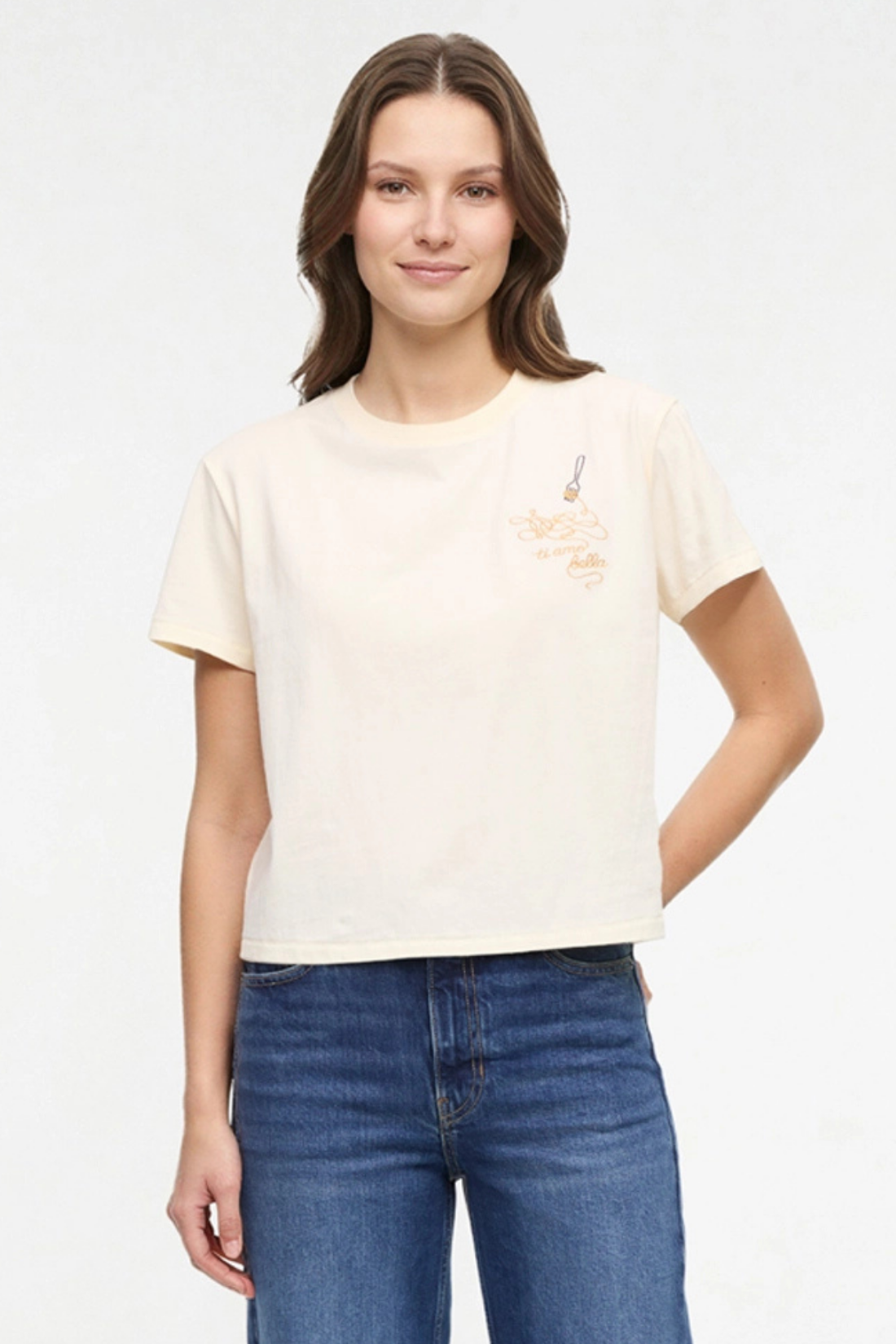 Front view of woman wearing a pale yellow t-shirt with a small chest embroidered design of spaghetti and a fork graphic on a white background.